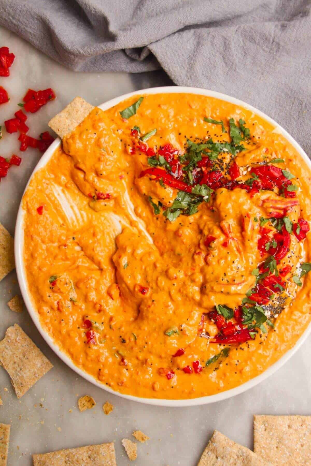 Cracker spread through a small white plate with red pepper hummus on it.