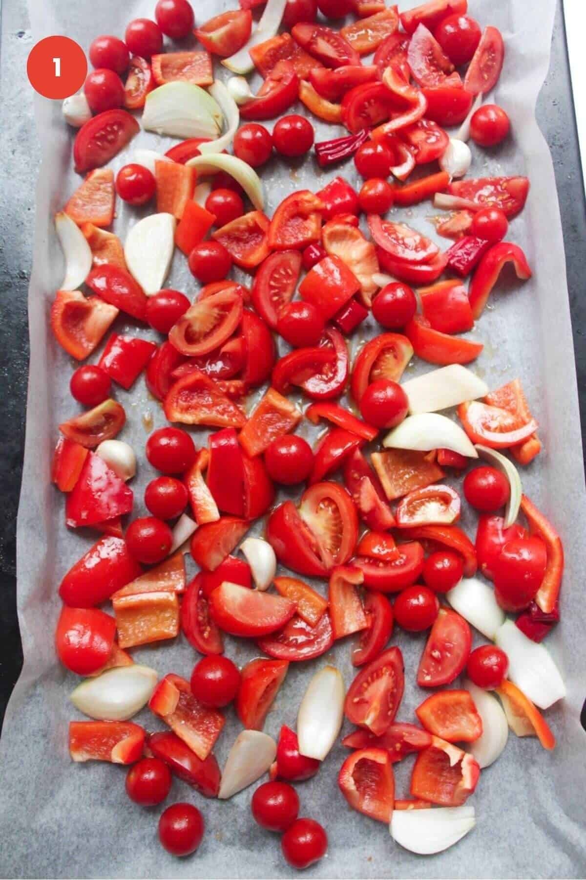Sliced tomatoes, bell peppers, garlic and onion on a baking sheet.