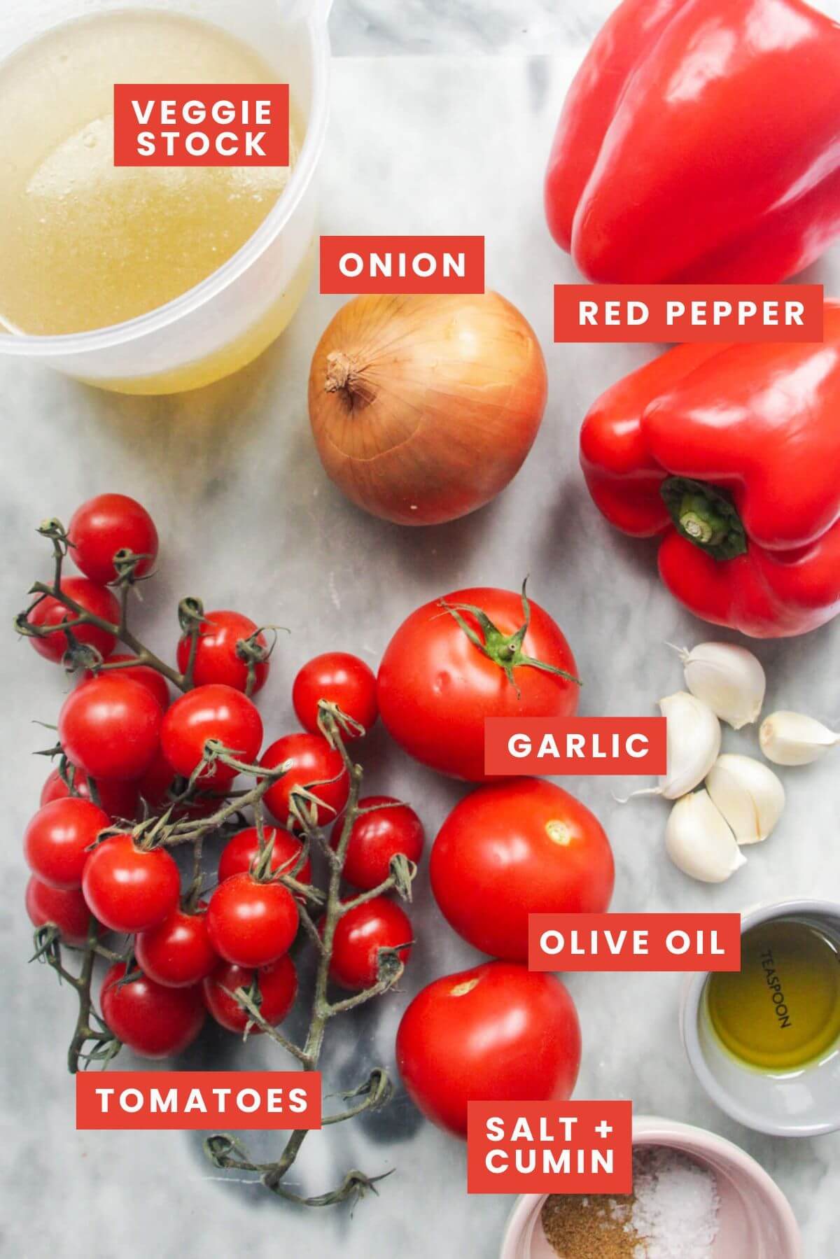 Ingredients for roasted tomato and red pepper soup laid out on a marble background.