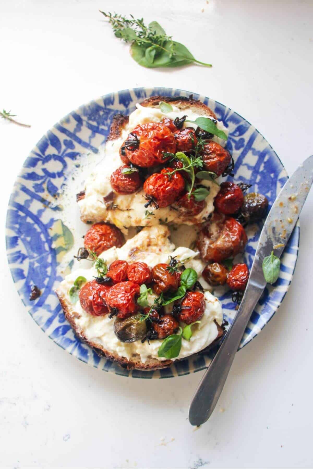 Roasted tomato and burrata toast sliced in half, on a white and blue plate.