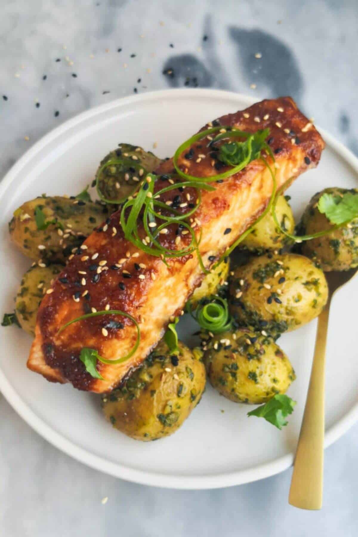 Piece of miso grilled salmon on a bed of herby potatoes on a small white plate.
