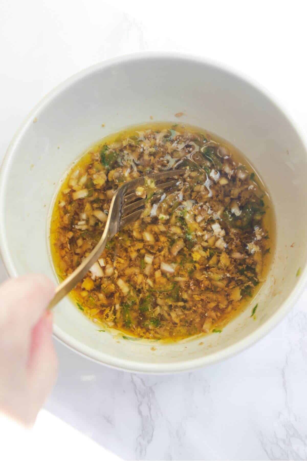 Mixing crudo dressing in a small white bowl with a gold fork.