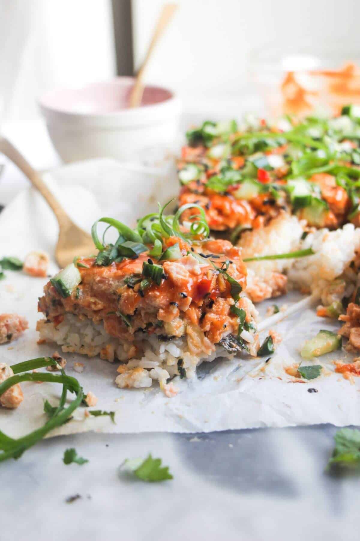 Close up of a piece of salmon sushi bake, with the rest of the bake in the background.