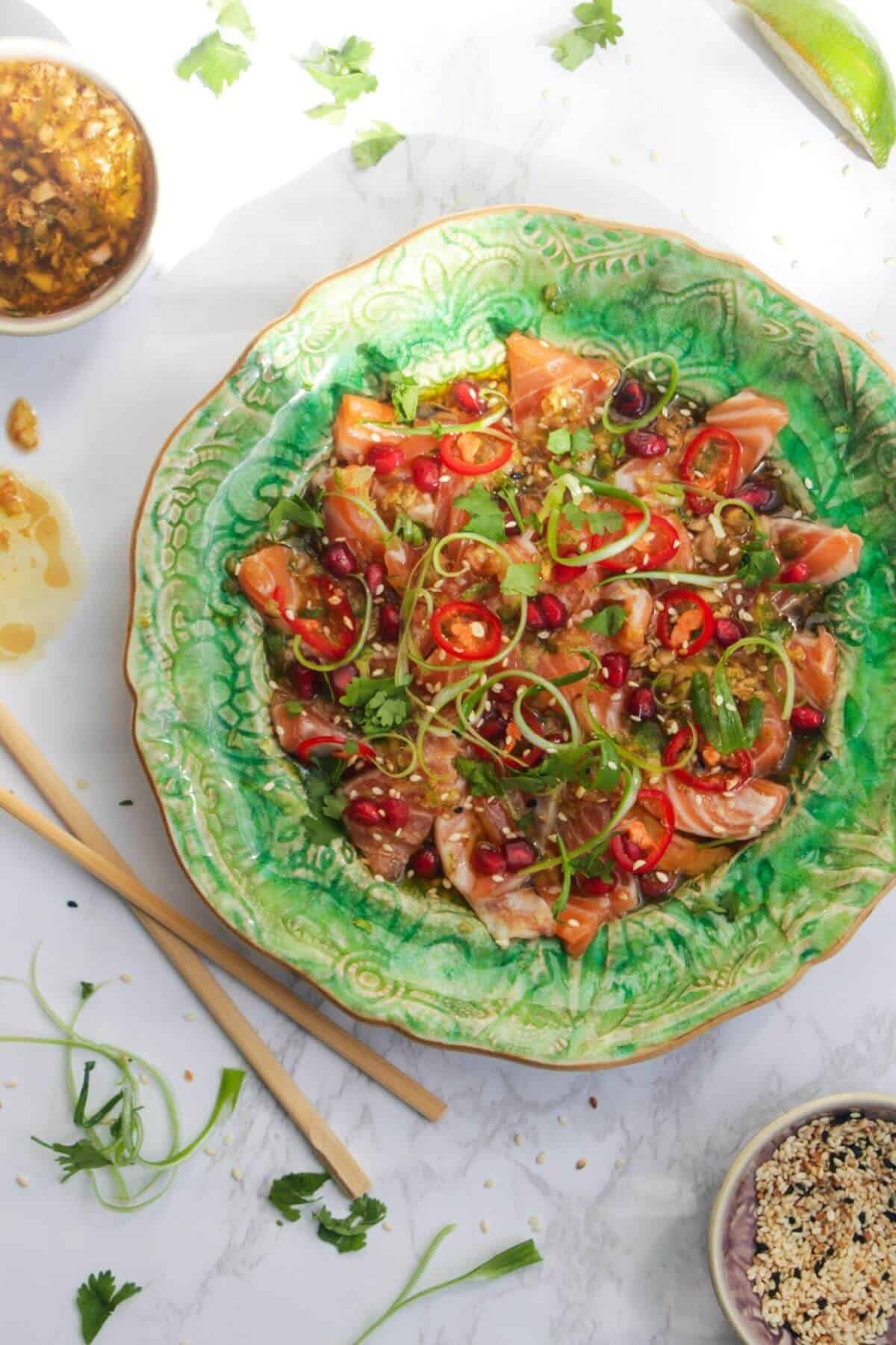 Salmon crudo on a small green plate with chopsticks and lime on the side.