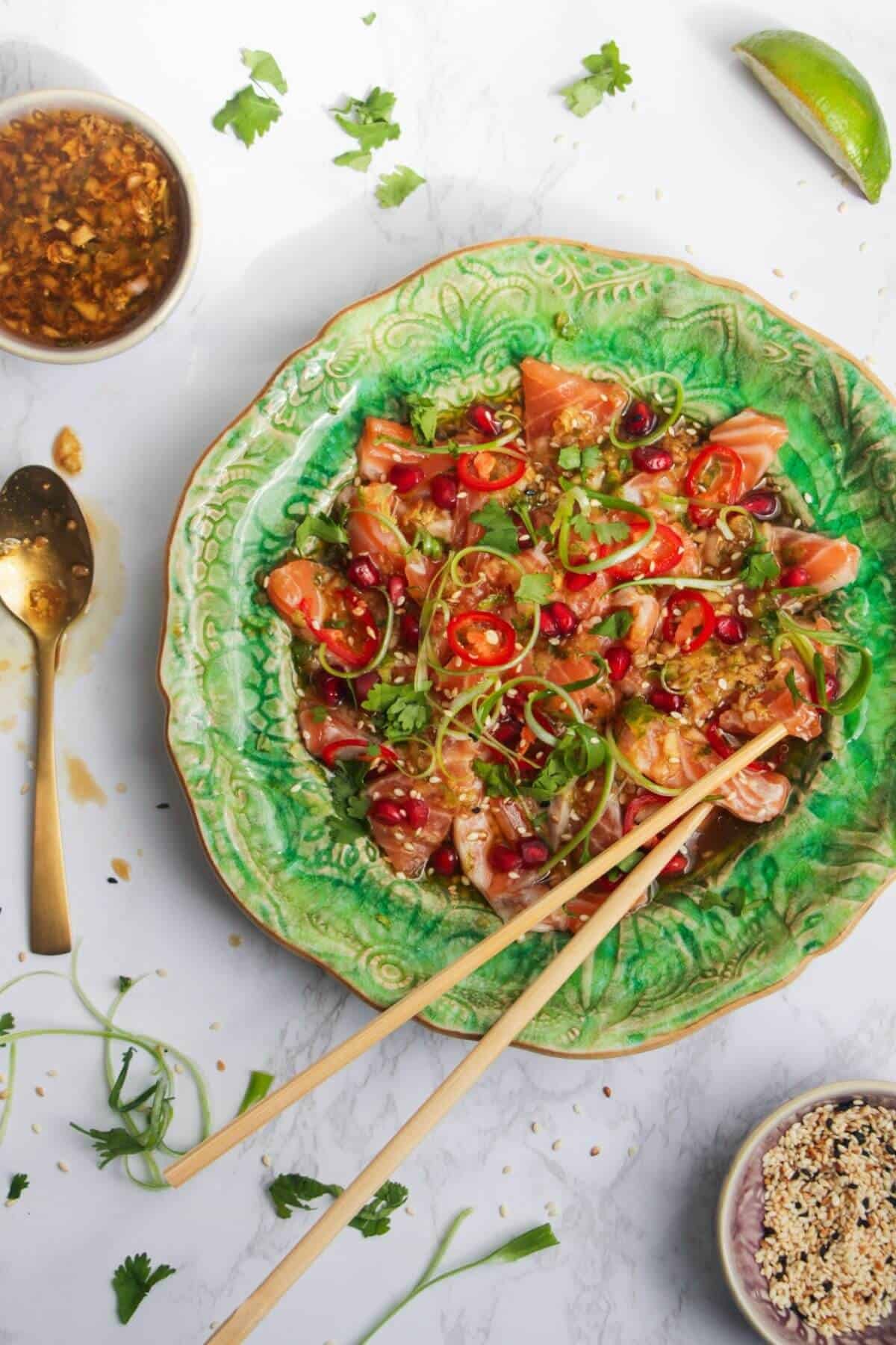 Salmon crudo on a small green plate with chopsticks and lime on the side.