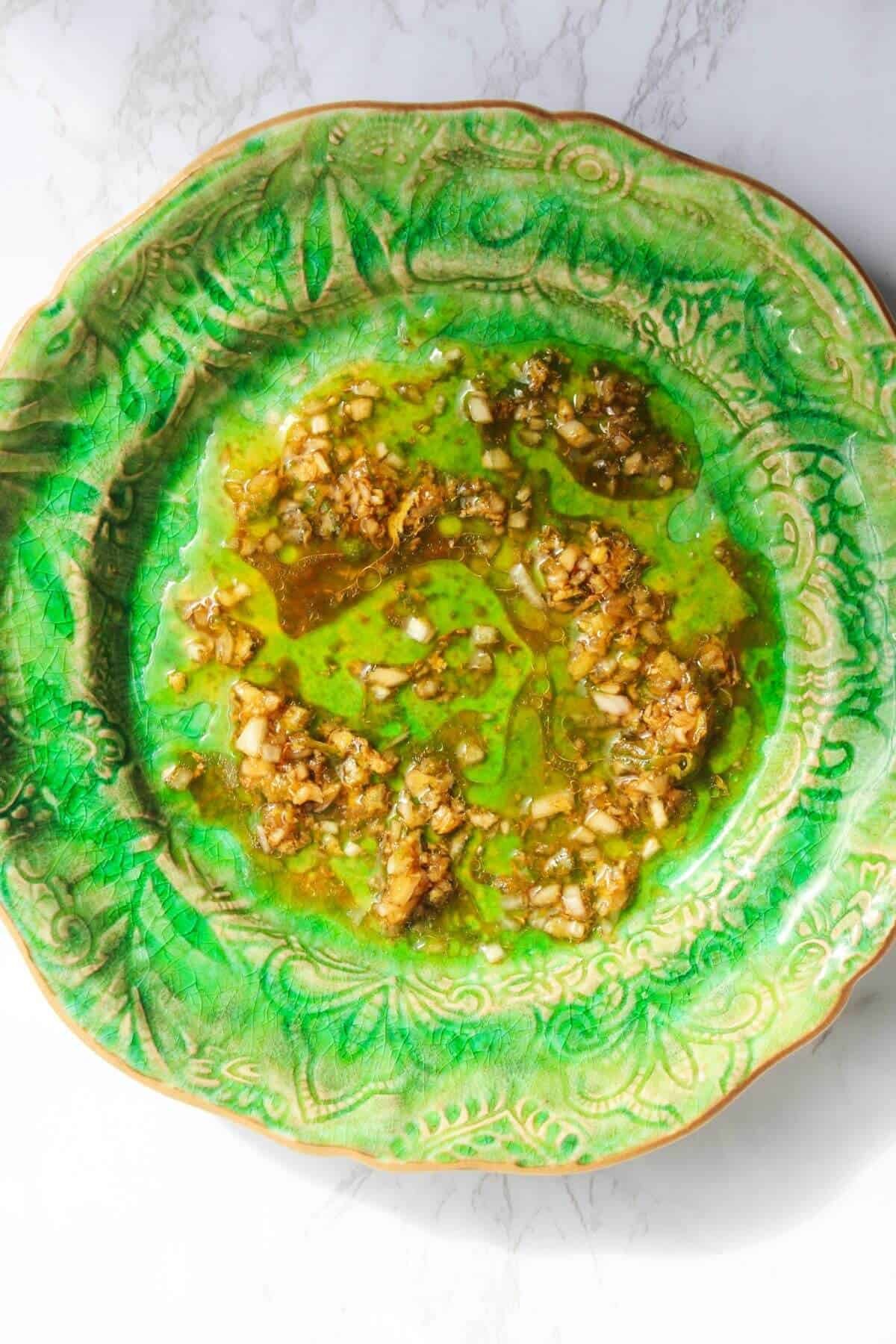 Dressing on a small green plate on a white marble background.