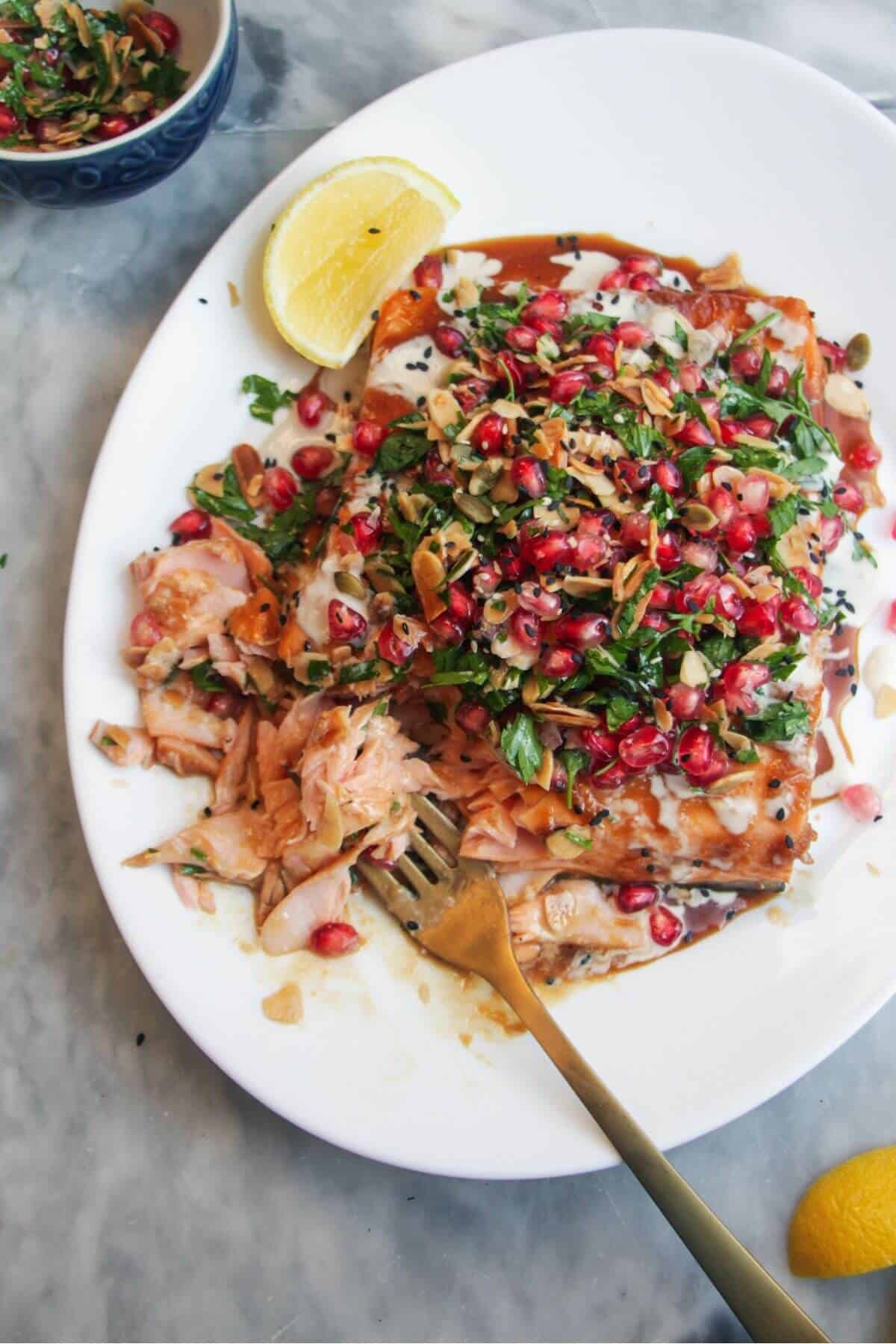 Maple miso glazed salmon fillet with pomegranate almond salsa, with lemon wedges on the side.