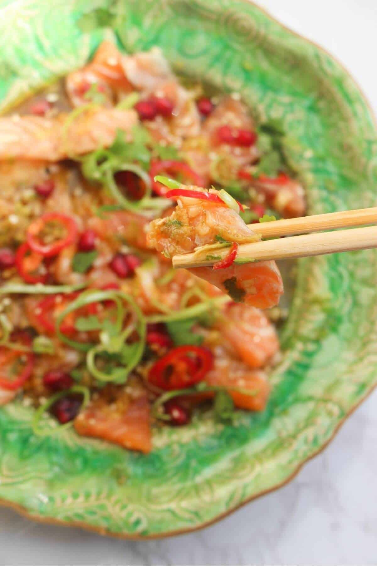 Close up of chopsticks holding up a piece of salmon crudo.