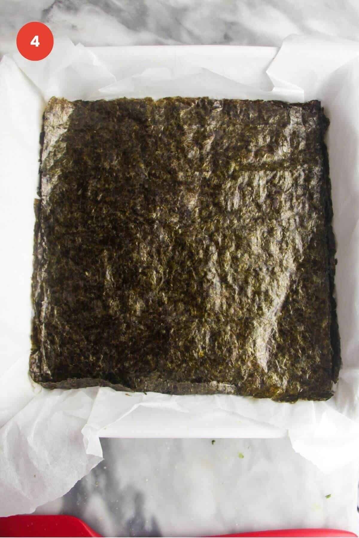 Nori sheet placed on top of rice in baking dish.