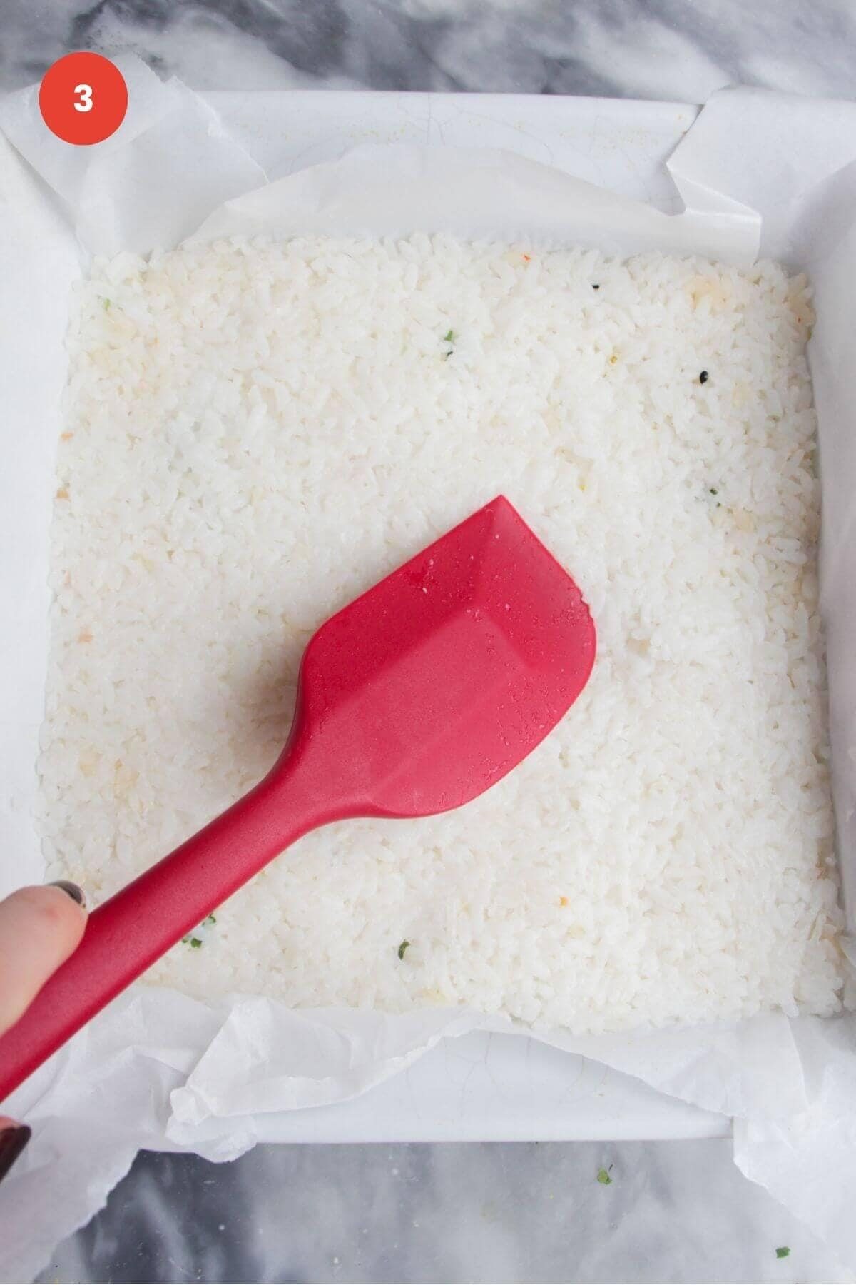 Spatula pressing rice into a baking dish.