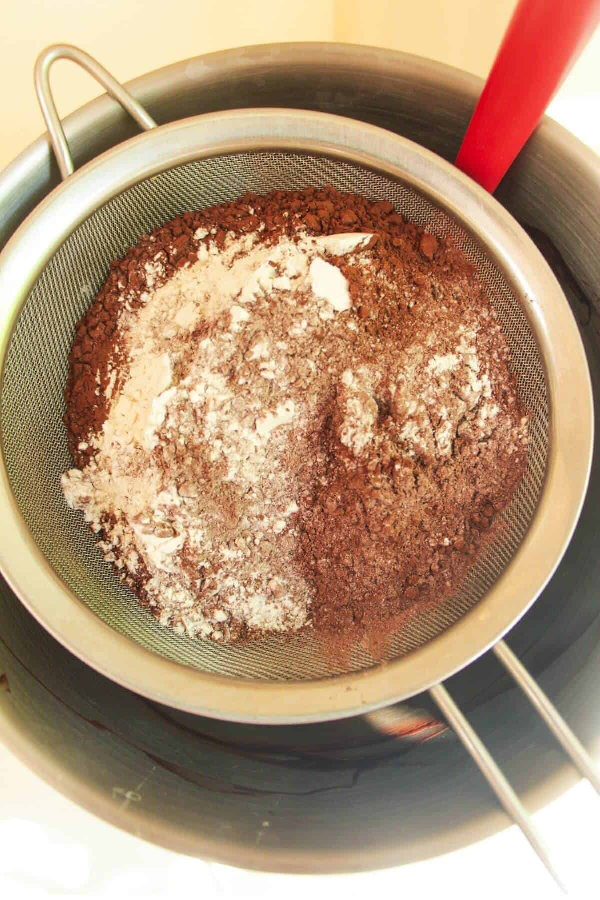Flour and cocoa powder in a sieve over a large mixing bowl.