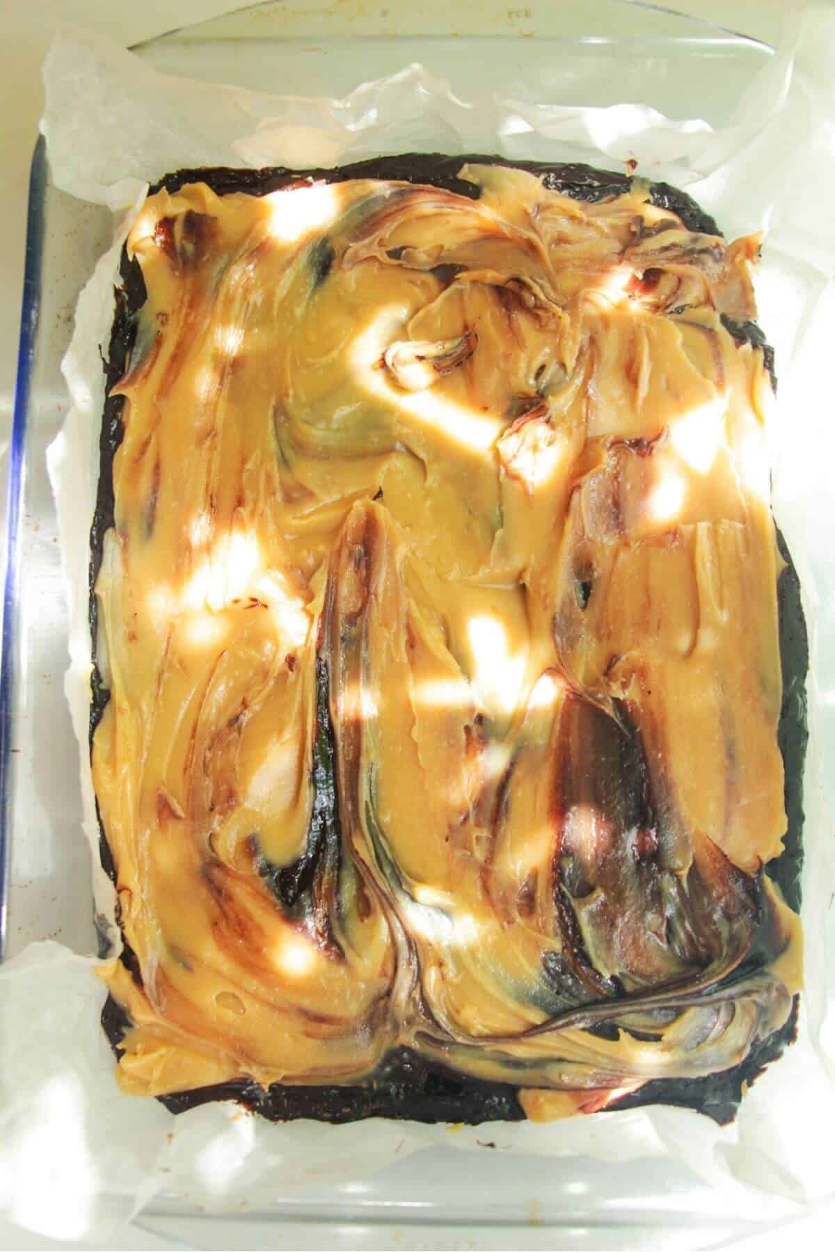 Salted caramel layered on top of brownie batter in a lined oven dish.