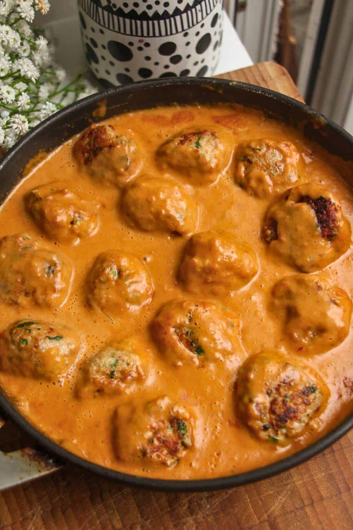 Chicken meatballs simmering in a satay sauce.