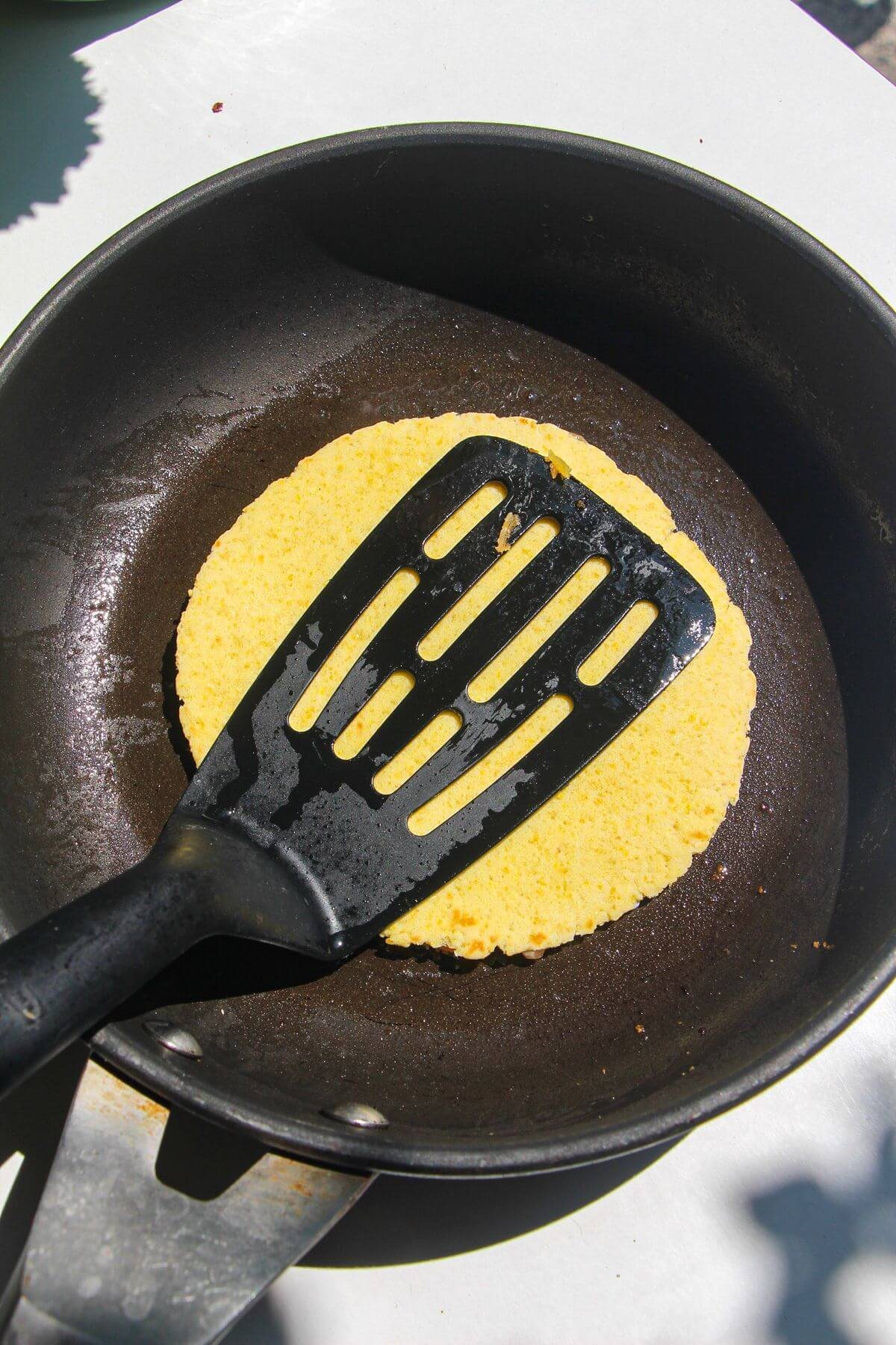 Spatula pressing down on tortilla in pan.