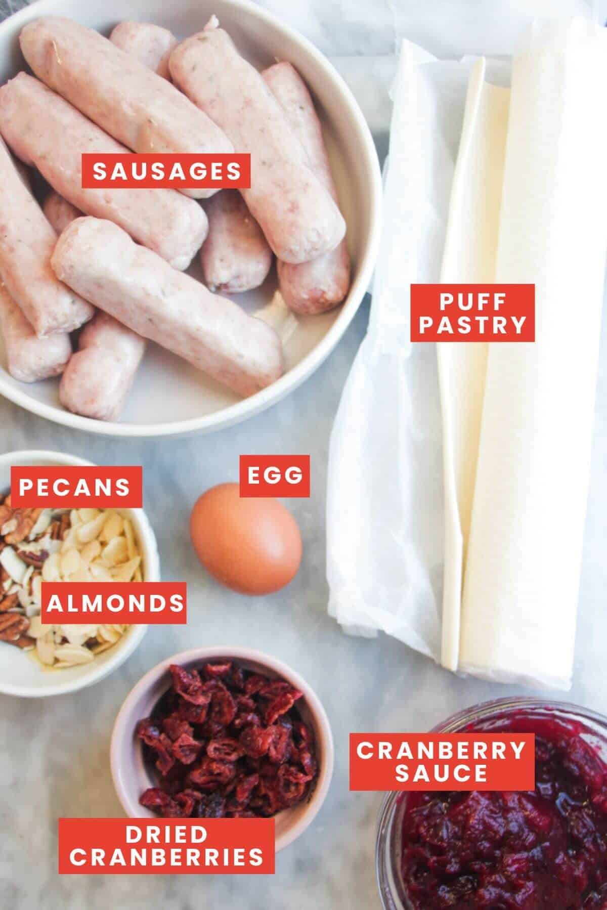 Ingredients for Christmas sausage roll wreath laid out on a marble background and labelled.