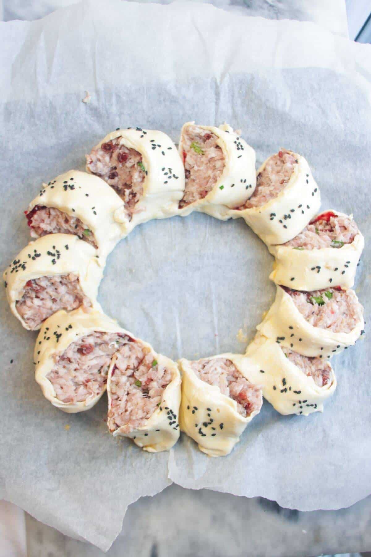 Sausage roll wreath egg-washed and sprinkled with black sesame seeds, ready to be baked.