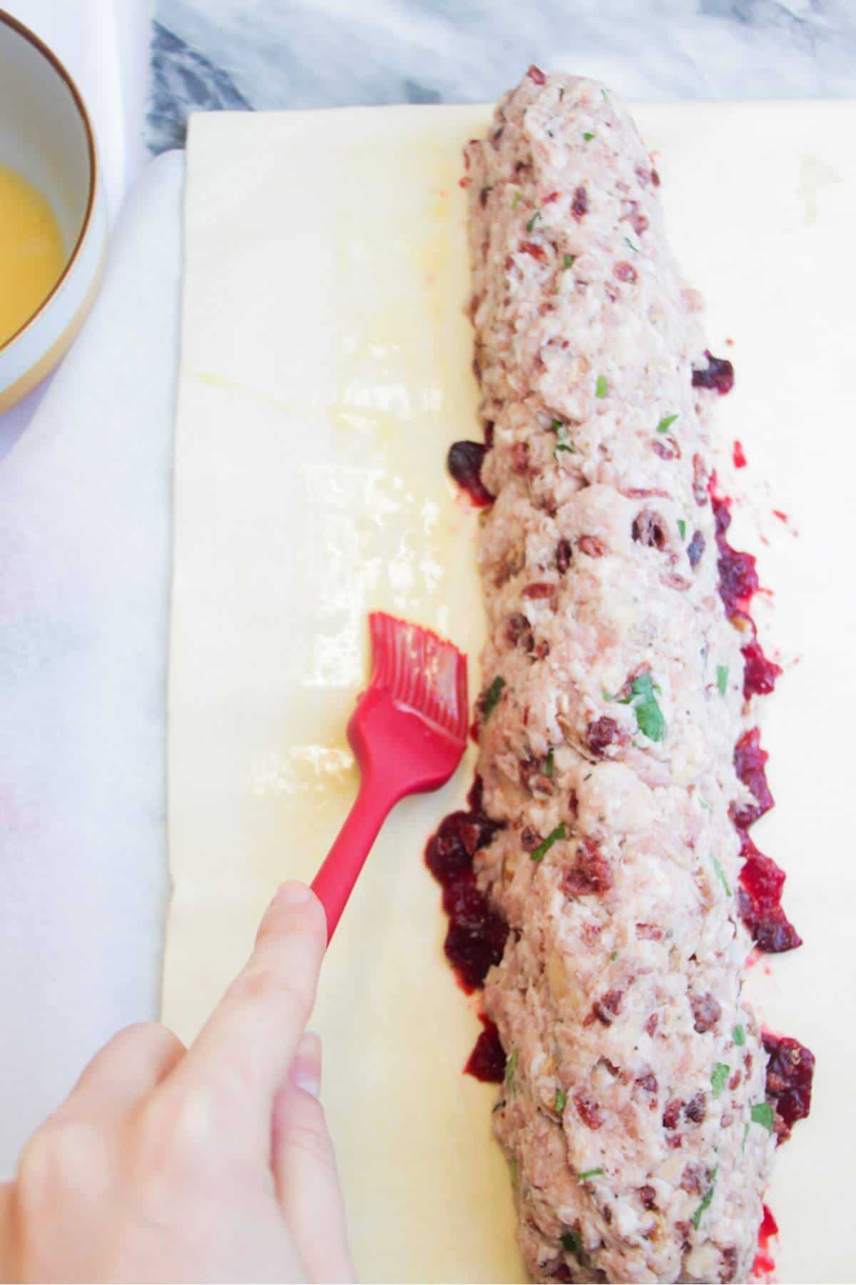 A red pastry brush brushing puff pastry with egg wash.