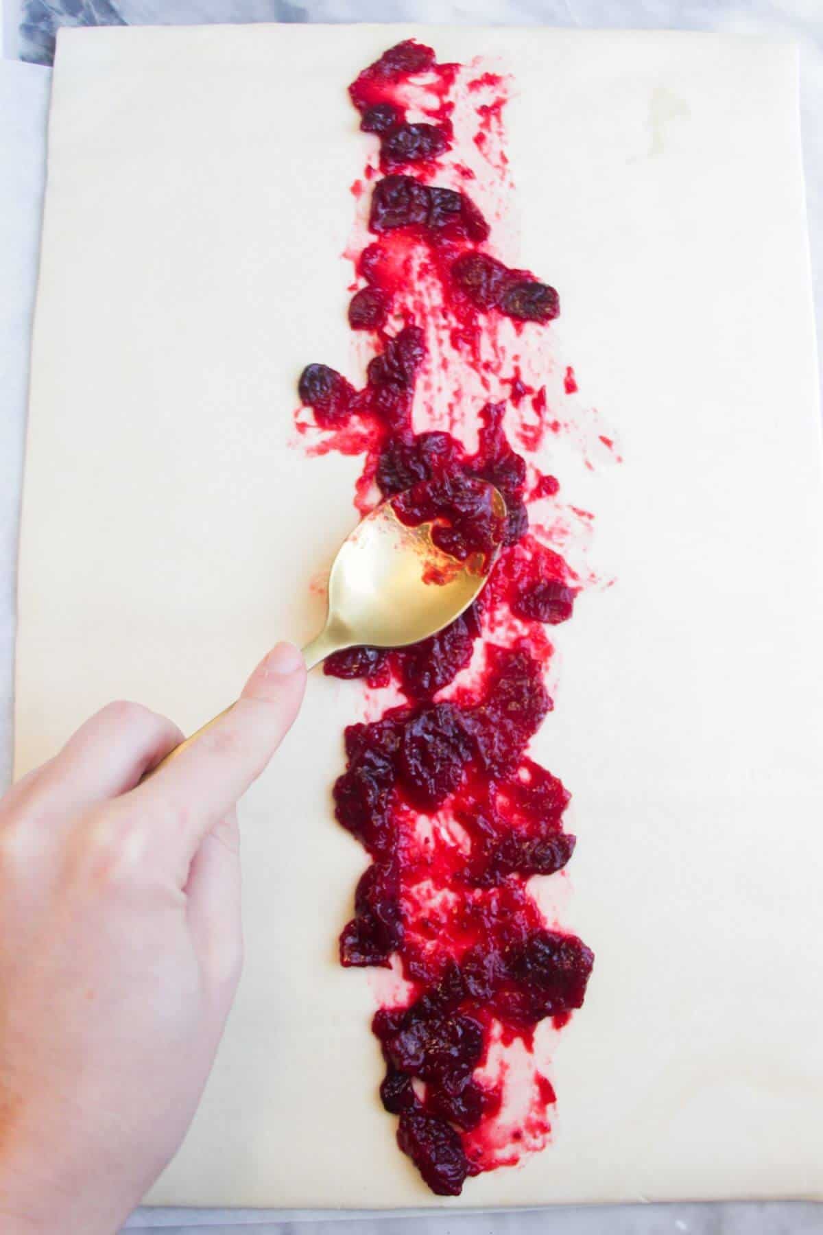 Spooing cranberry sauce down the middle of a puff pastry sheet.