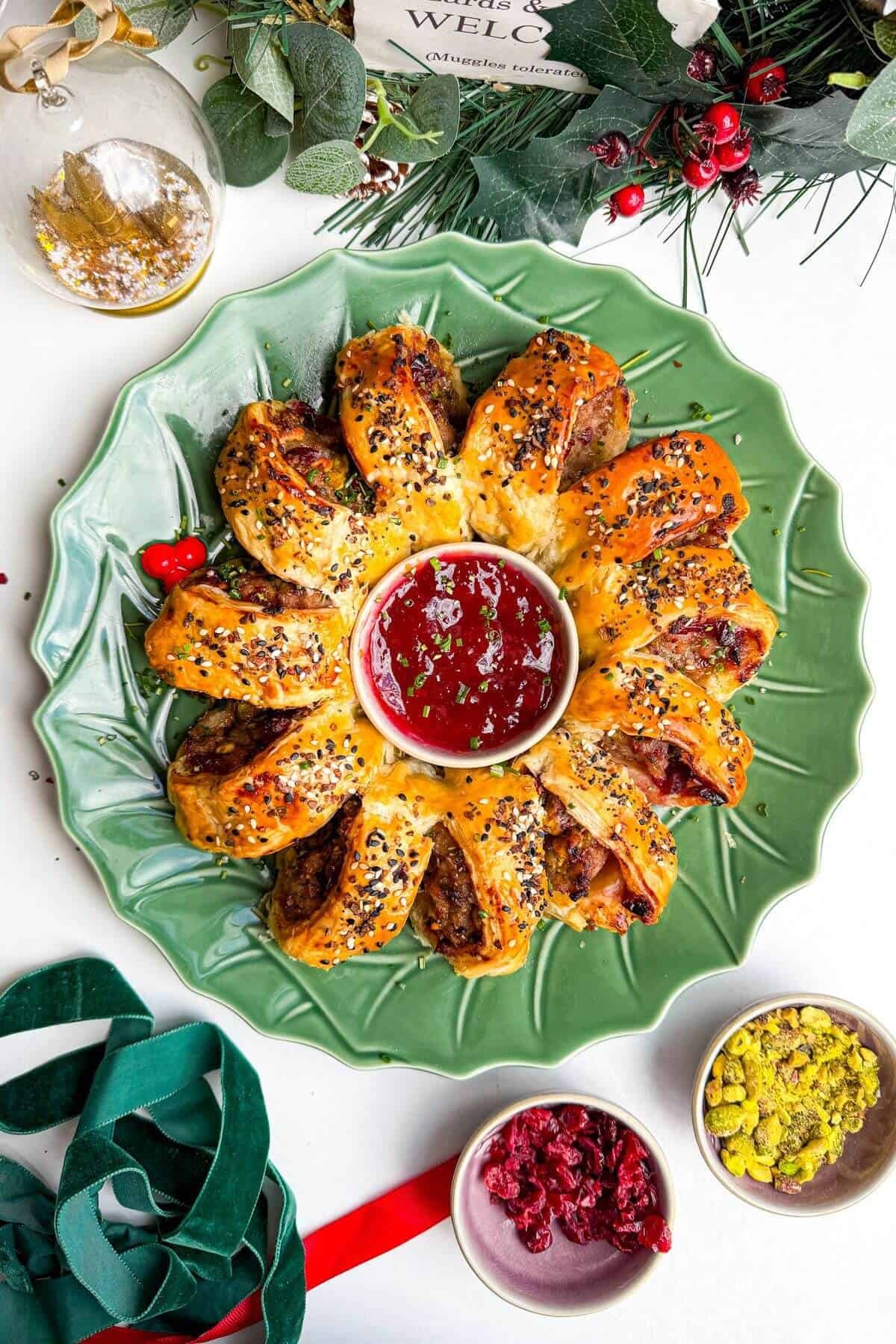 Sausage roll wreath on a plate with cranberry sauce in the middle.
