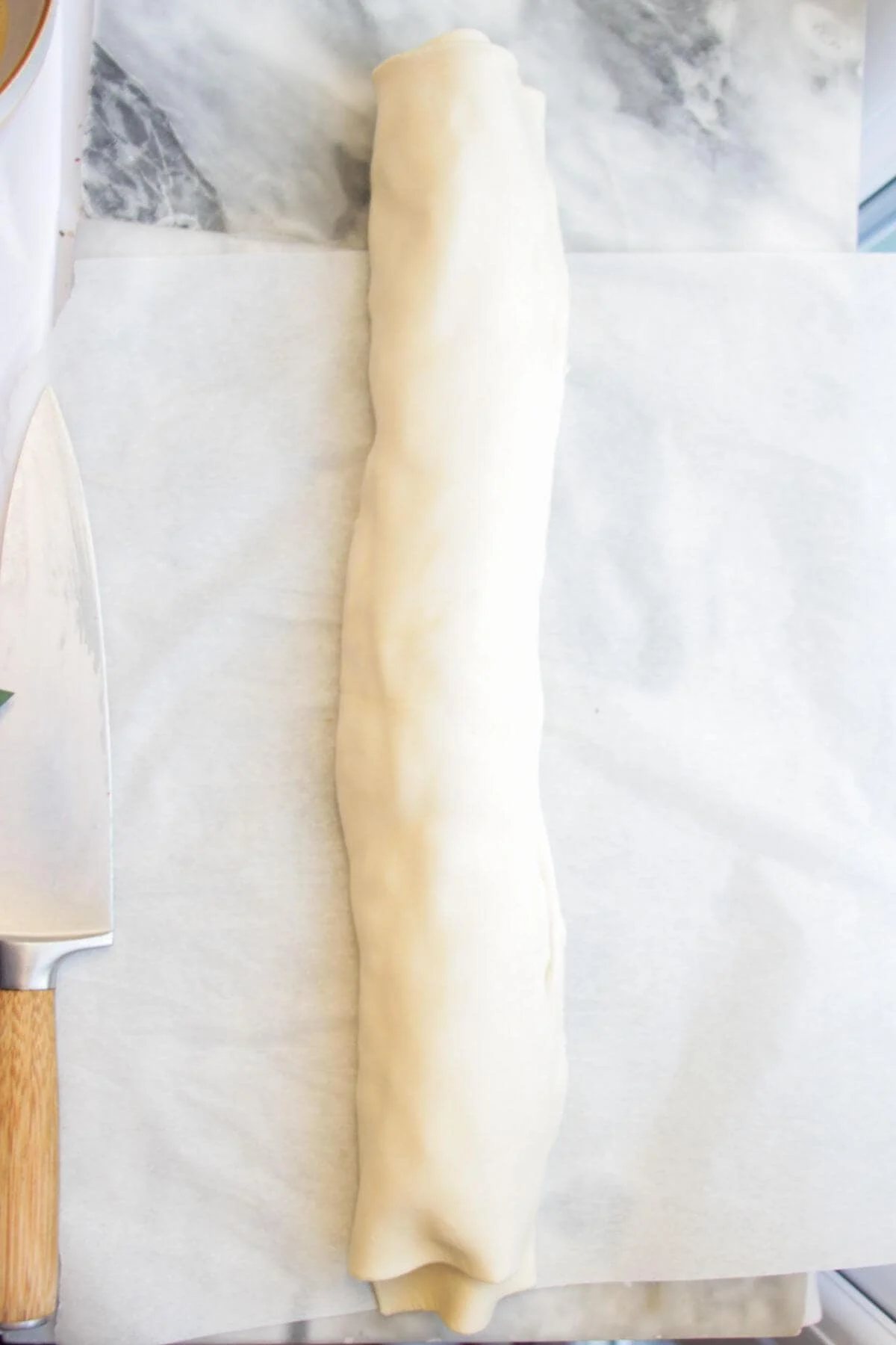 Long sausage roll formed on a baking paper lined surface.