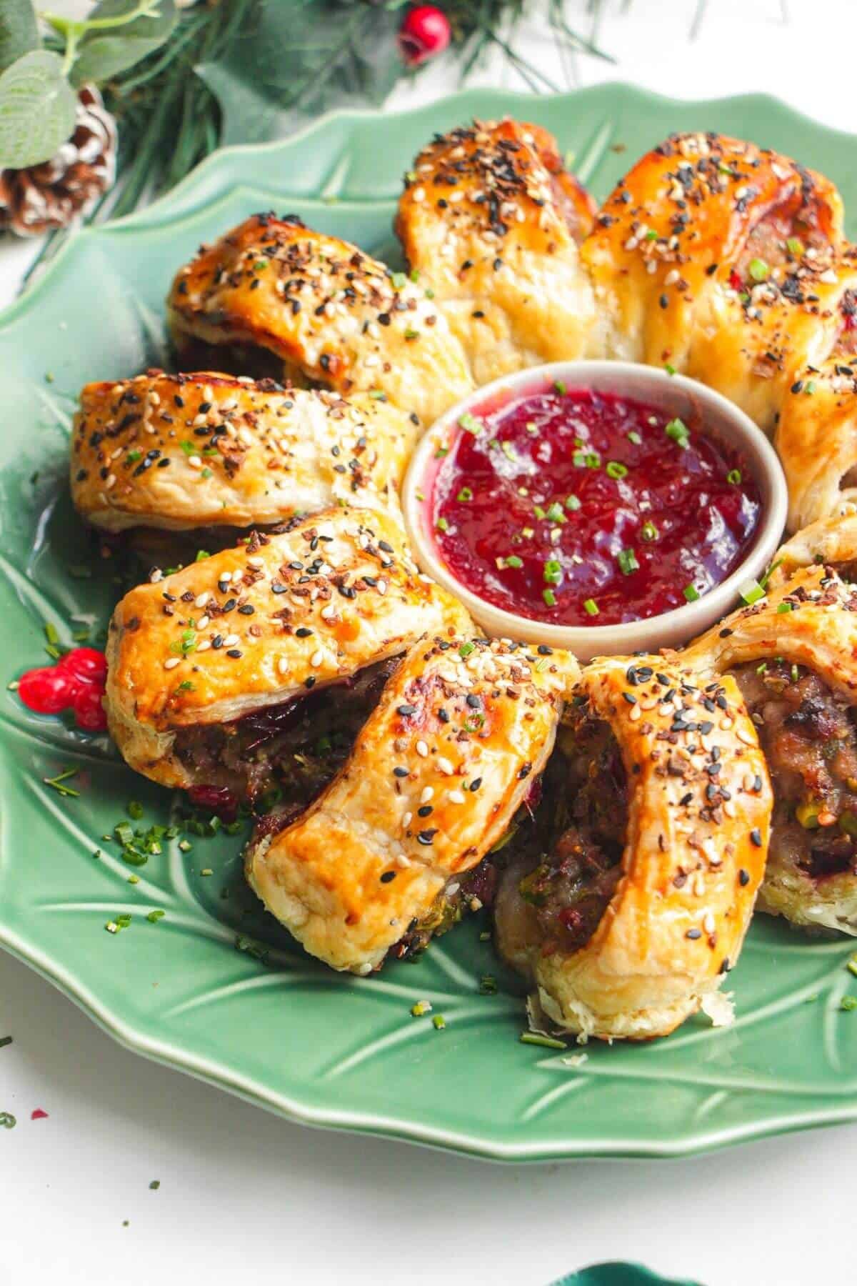 Sausage roll wreath on a plate with cranberry sauce in the middle.