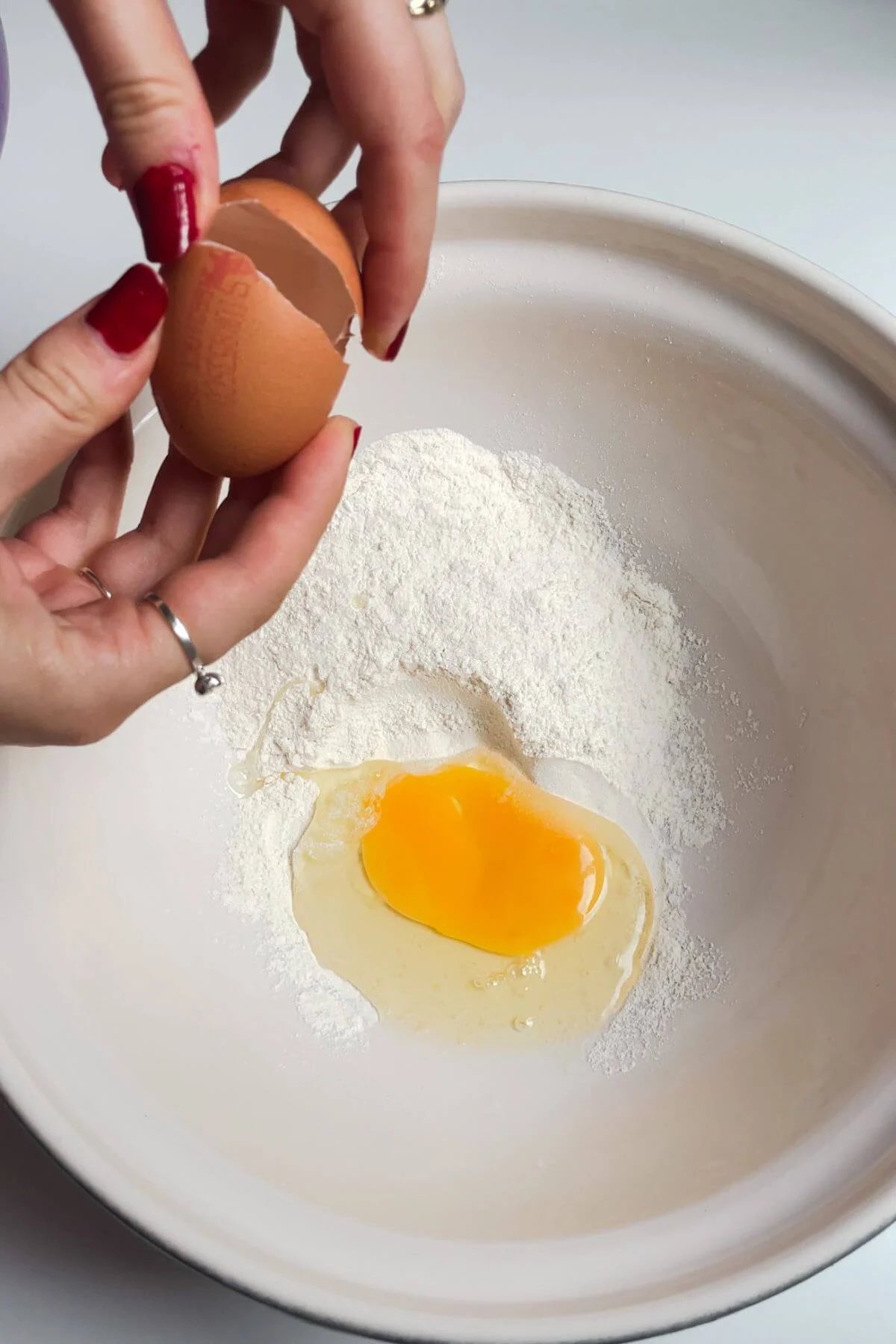 Hands cracking an egg into a white bowl with flour inside.