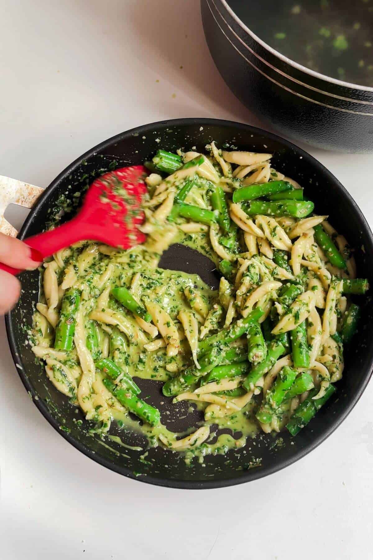 Red spatula stirring pesto through scissor cut pasta and beans.