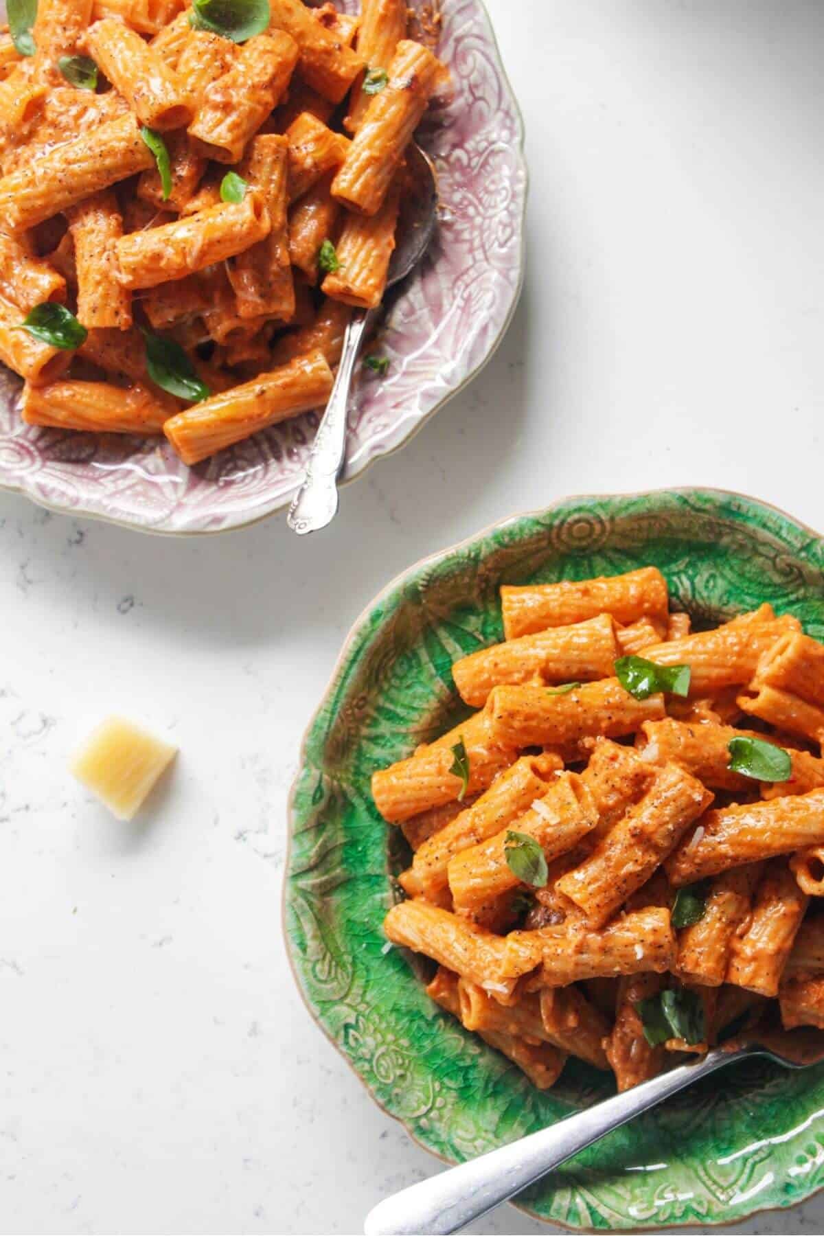 Two plates of spicy rigatoni on a white marble background.