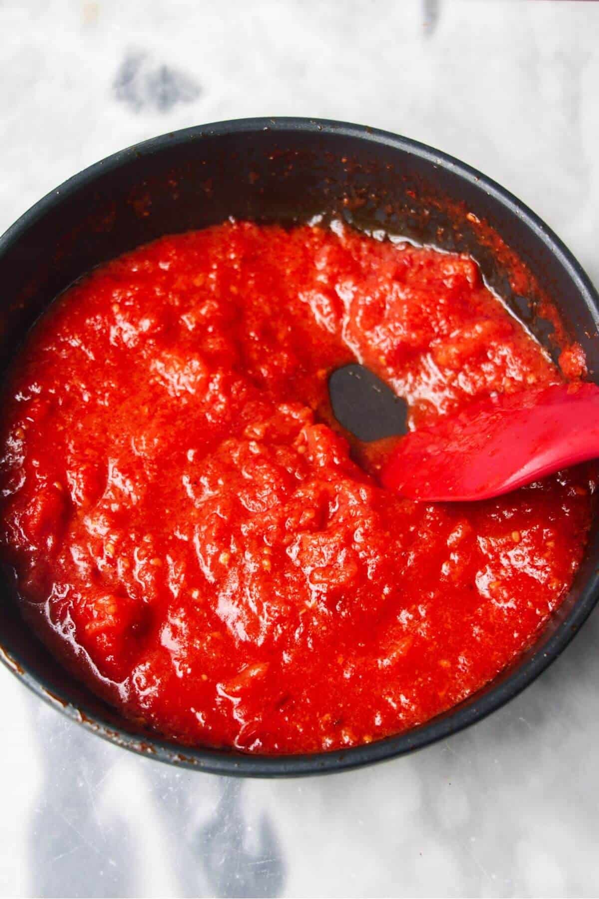 Thickened tomato sauce being stirred in a small black pan.