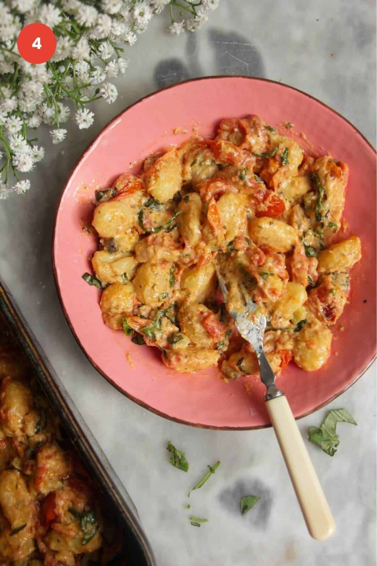 Creamy gnocchi served up in bowl with baking dish on the side.
