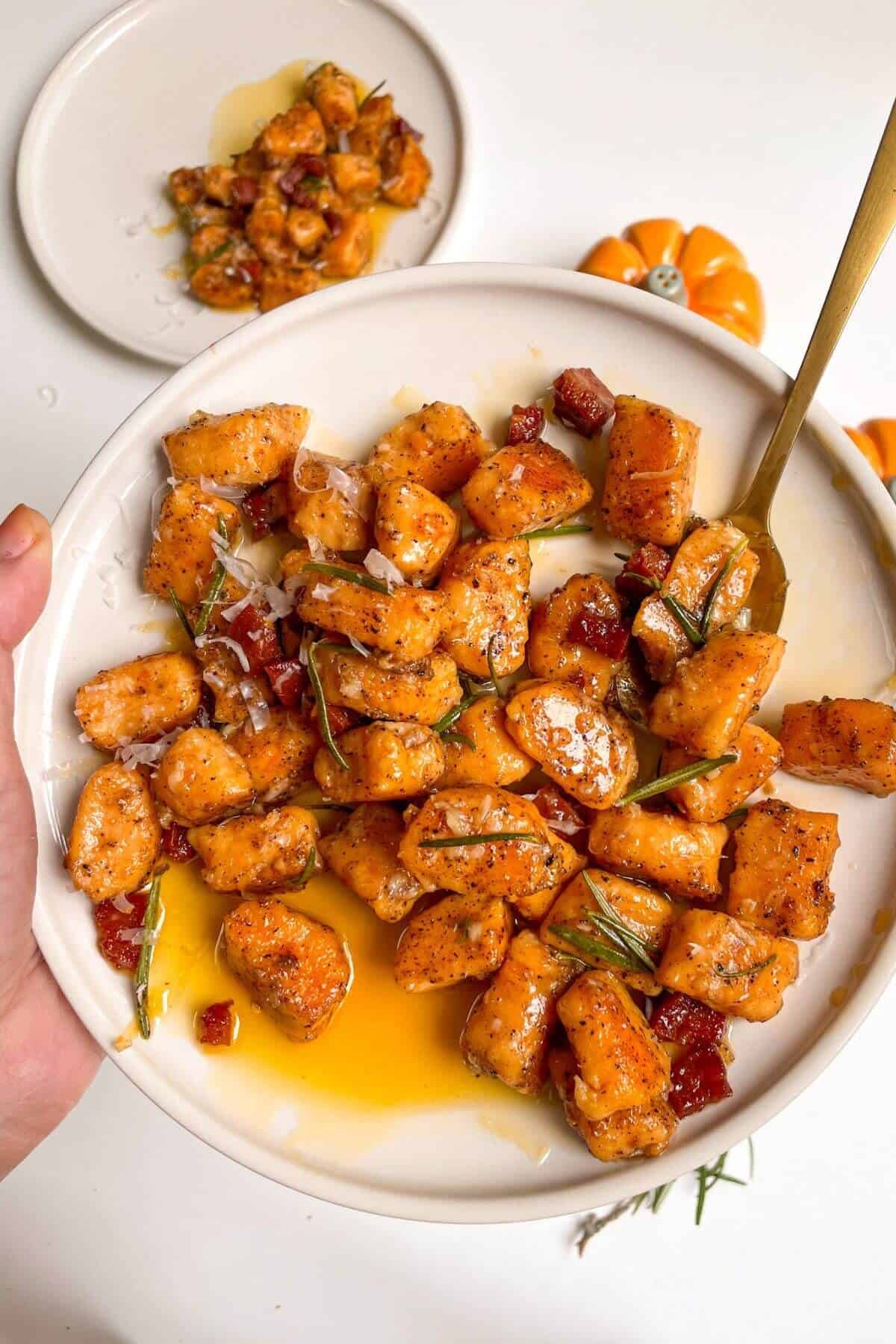Hand holding a plate of sweet potato gnocchi with a gold spoon in it.