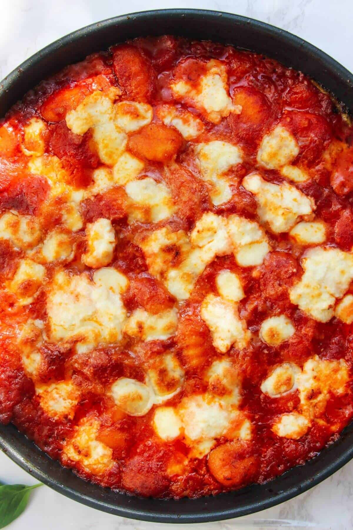 Close up of cheesy gnocchi baked in tomato sauce in a small frying pan.