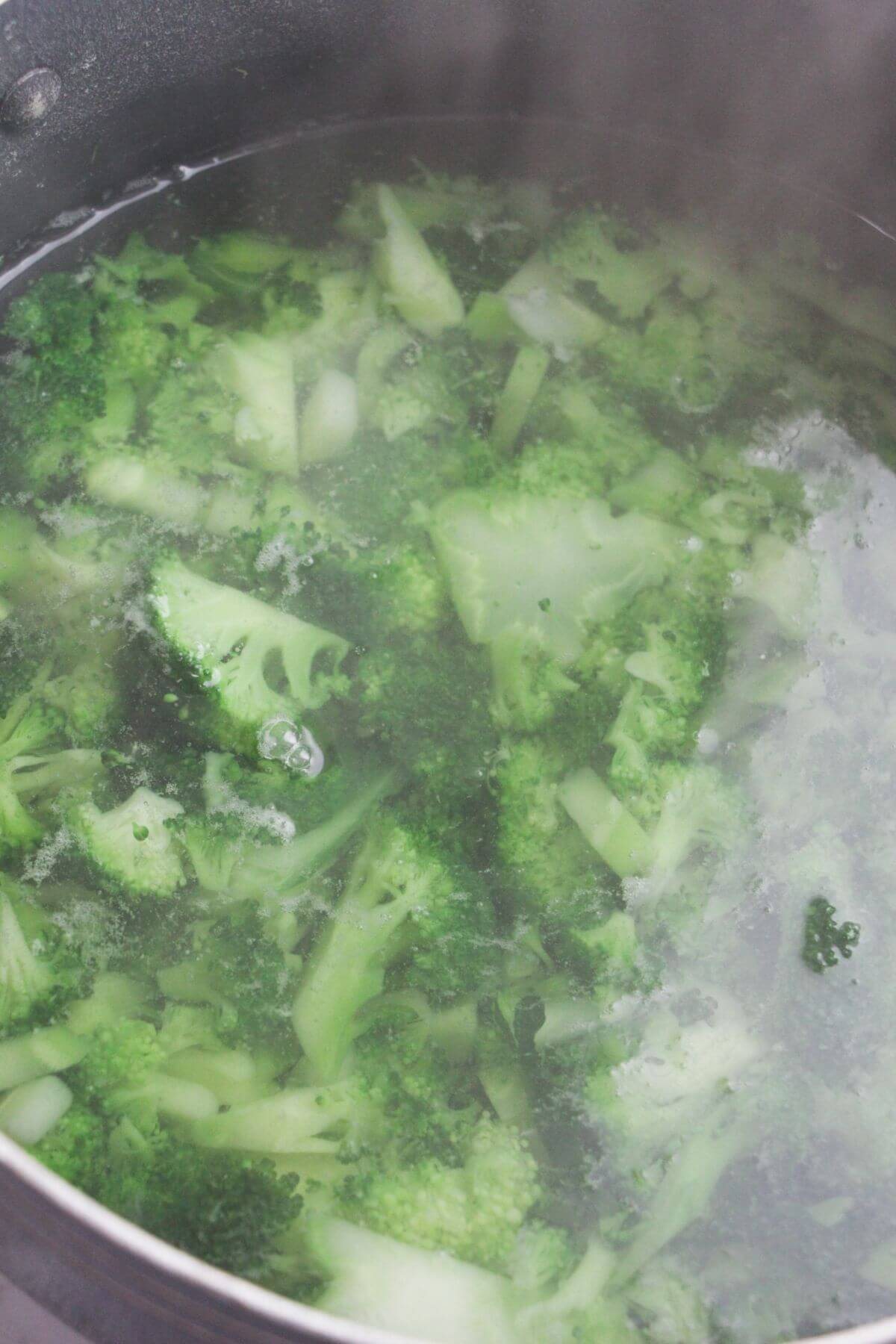 Broccoli florets cooking in a large pot of boiling water.