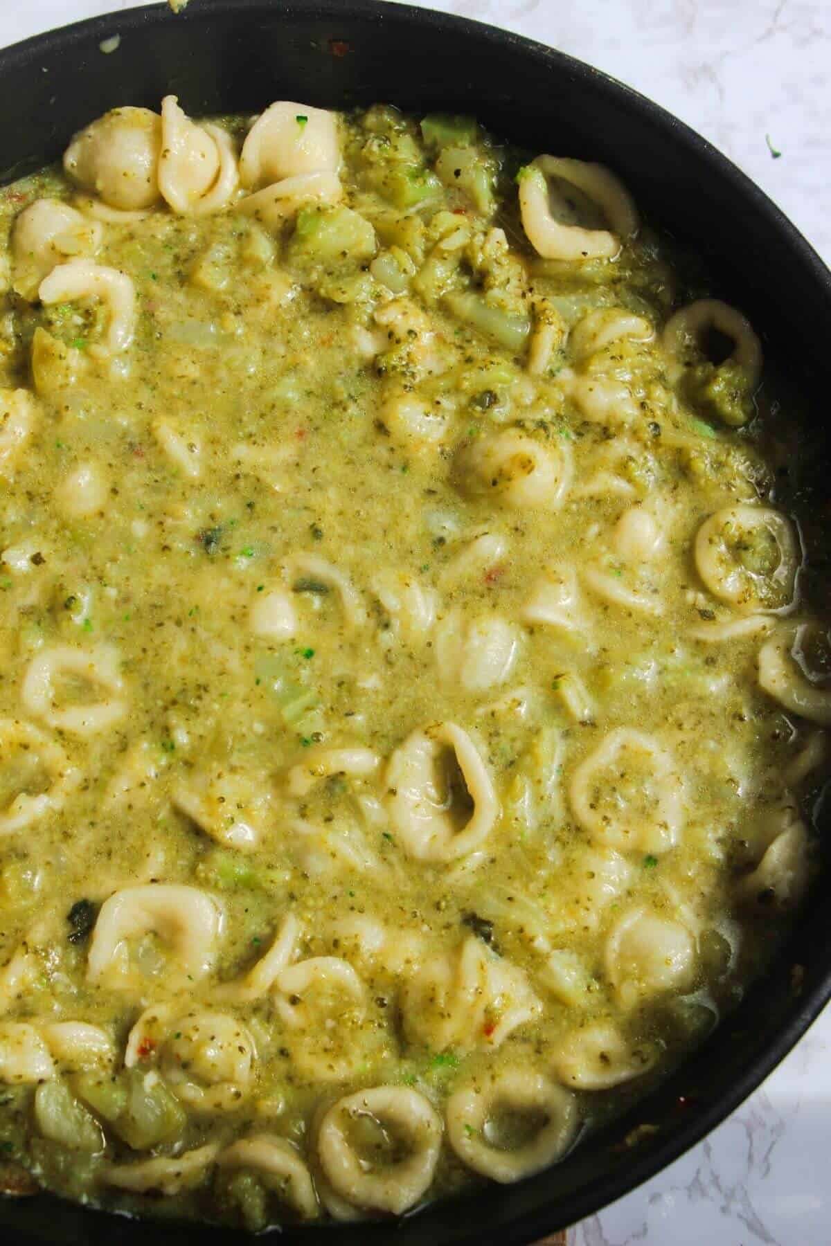 Pasta stirred through broccoli sauce in a large pan.