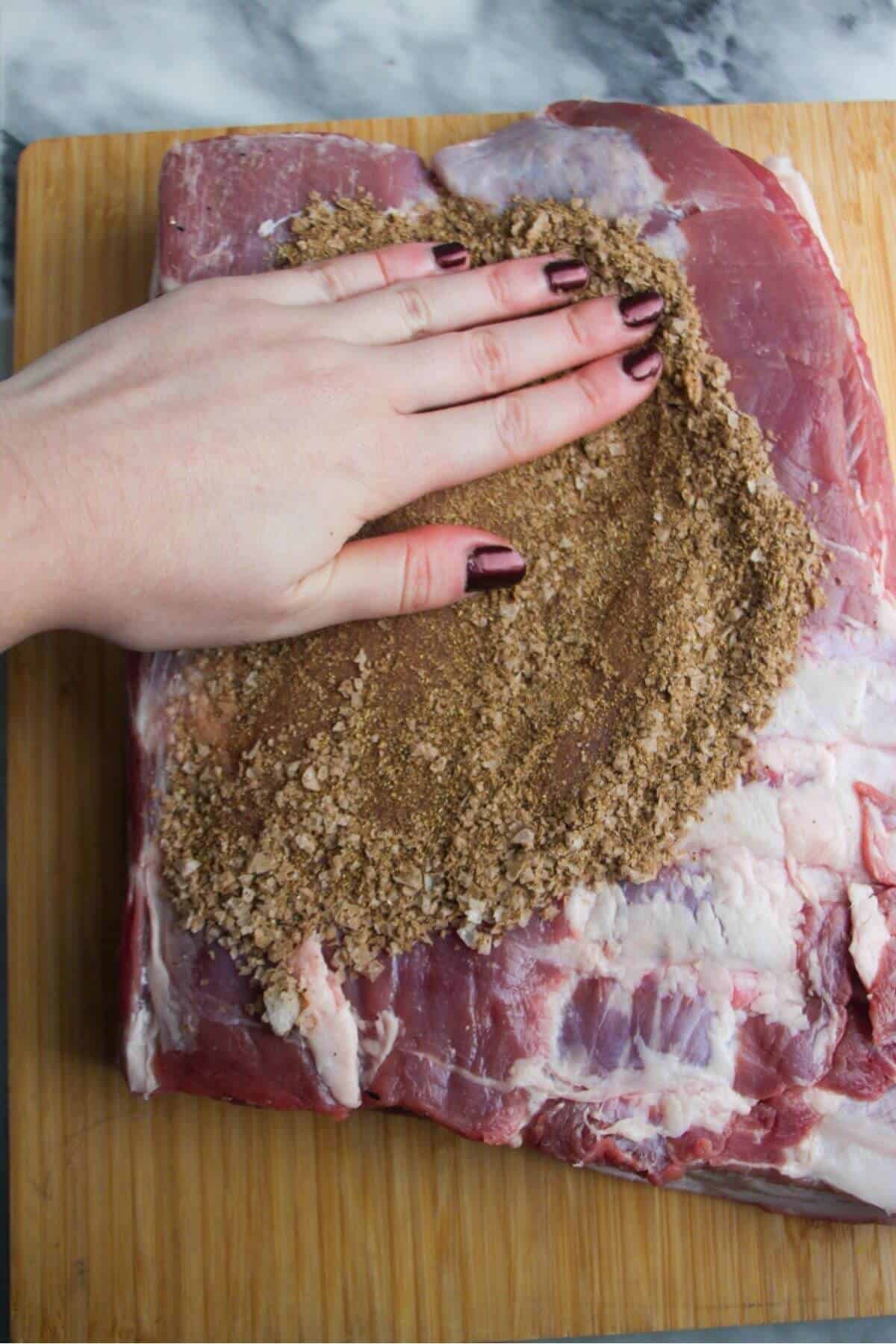 A hand rubbing Chinese 5 spice mix onto the flesh side of a large piece of pork belly.
