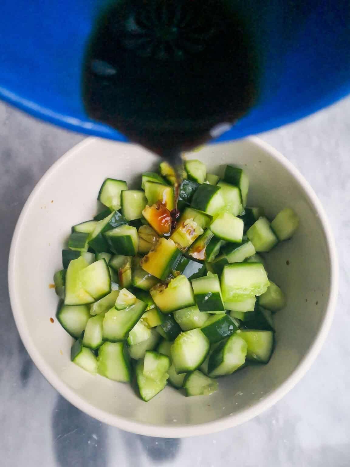 Pouring soy sauce into a small bowl filled with cucumber chunks.