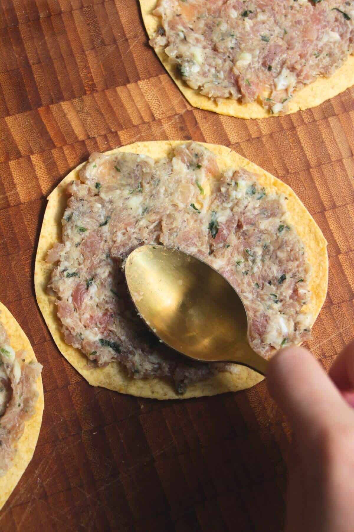 Back of a spoon pressing sausage meat onto a taco.