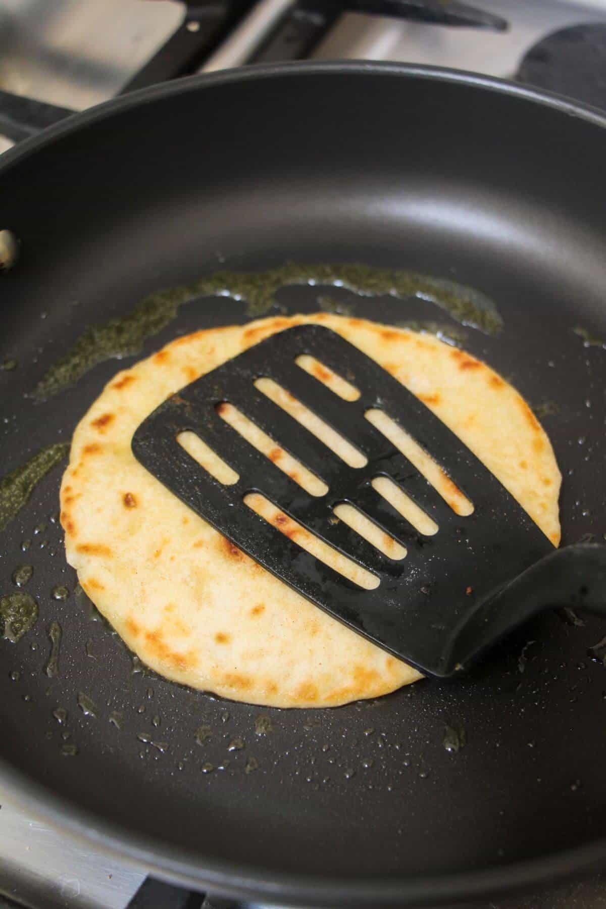 Black spatula pressing tortilla down in a small black pan.