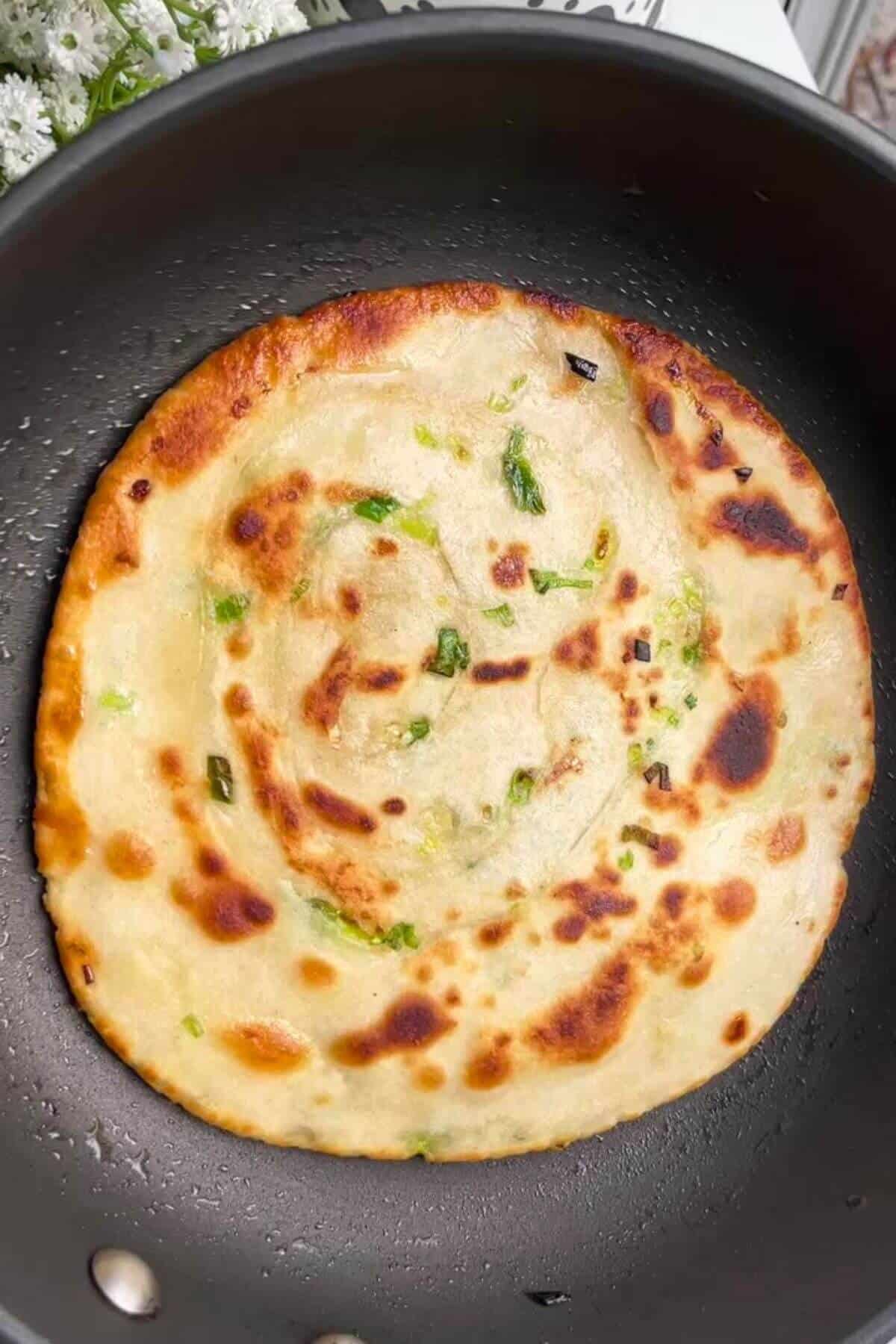 Scallion pancake cooking in a pan.