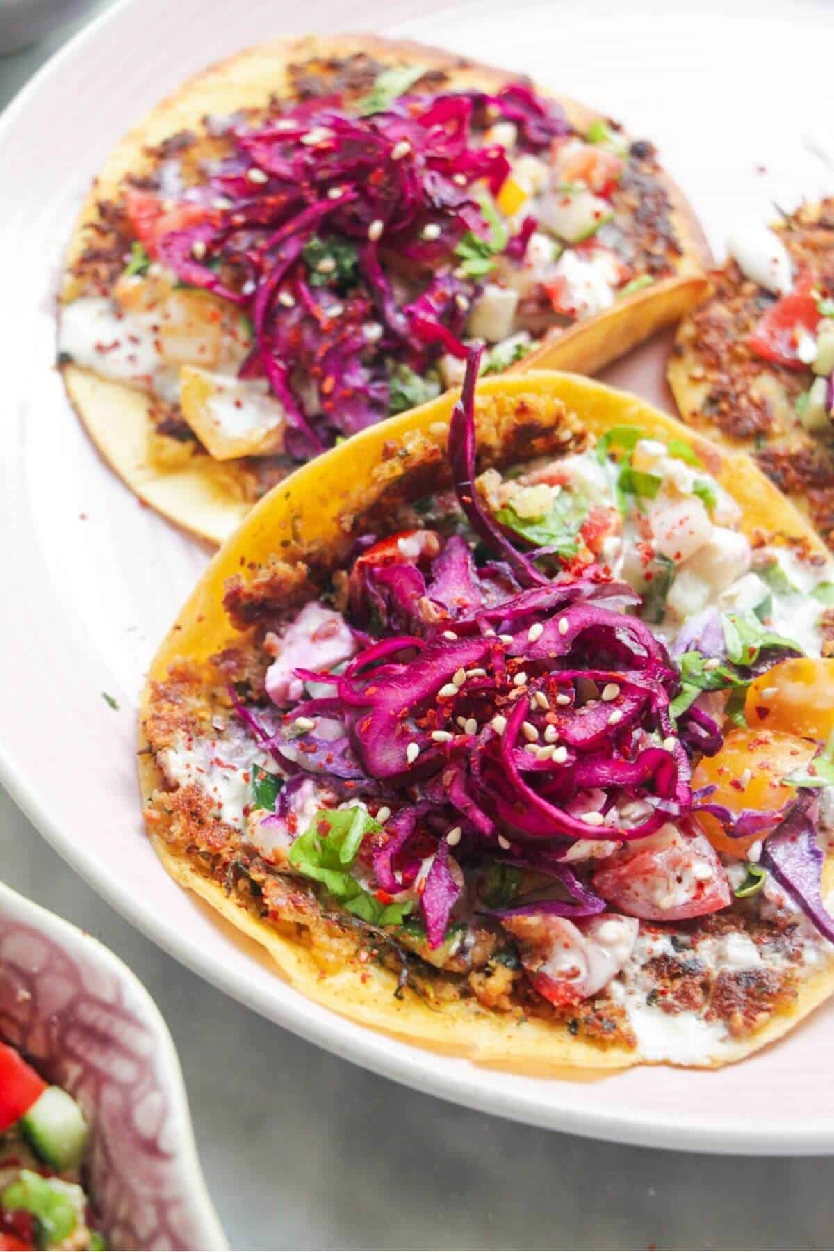 Four smash falafel tacos on a pink plate.