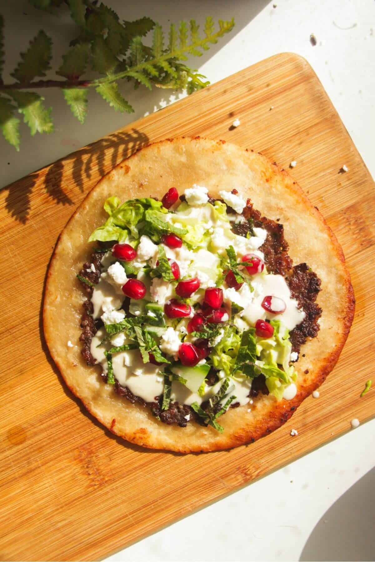 Smash kebab taco topped with pomegranate seeds and feta.