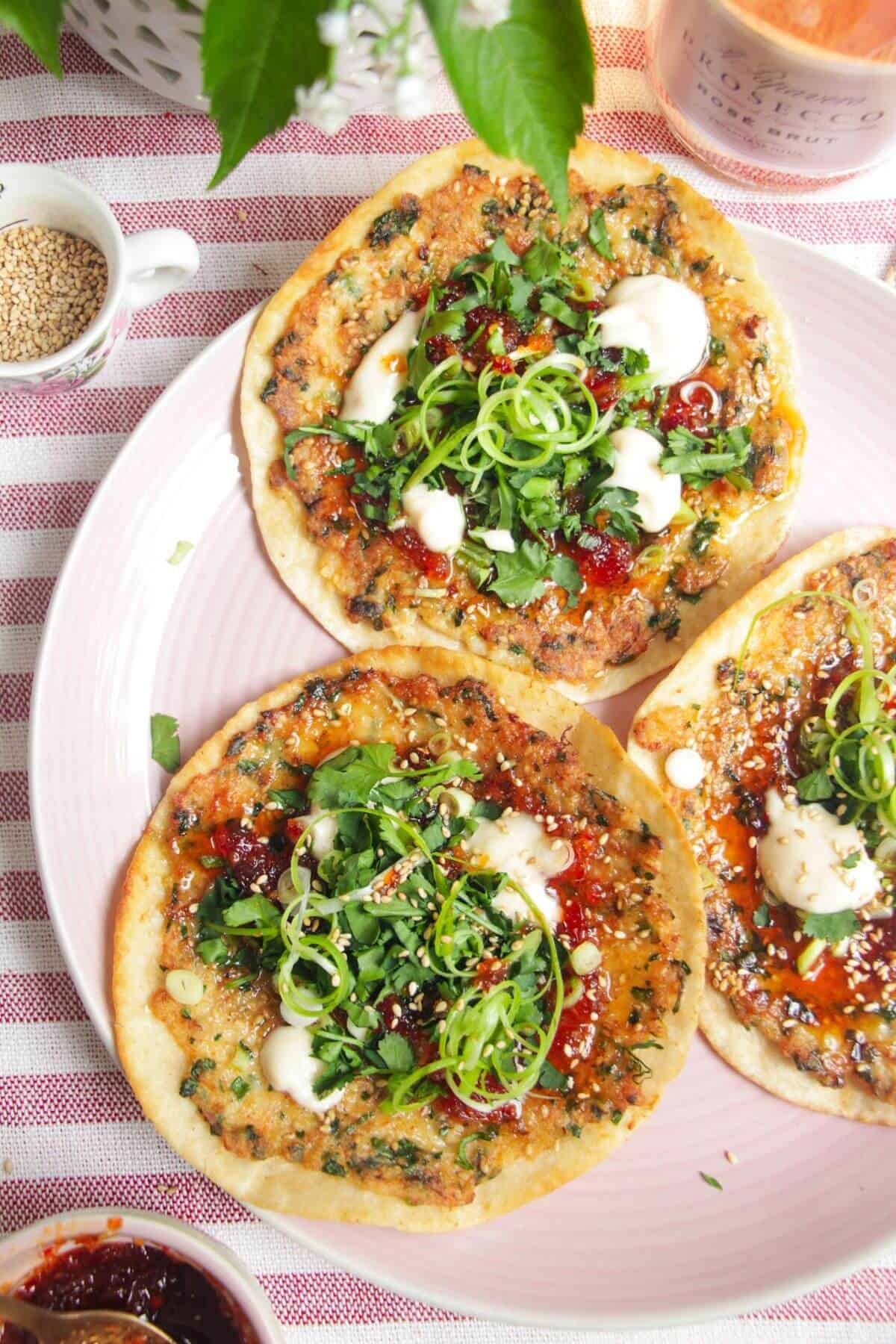 Three prawn toast tacos topped with herbs and aioli on a pink plate.