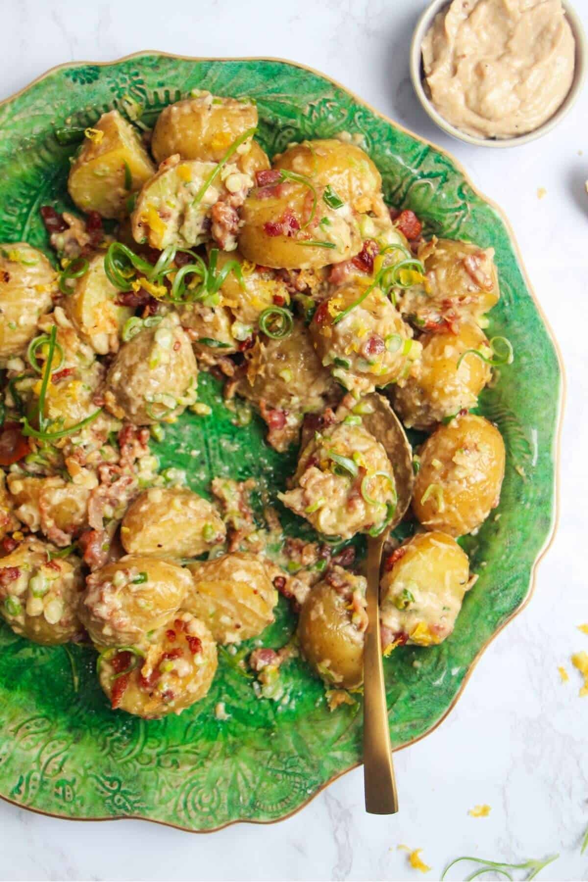 Close up of creamy Caesar potato salad on a large green serving plate with more Caesar dressing on the side.