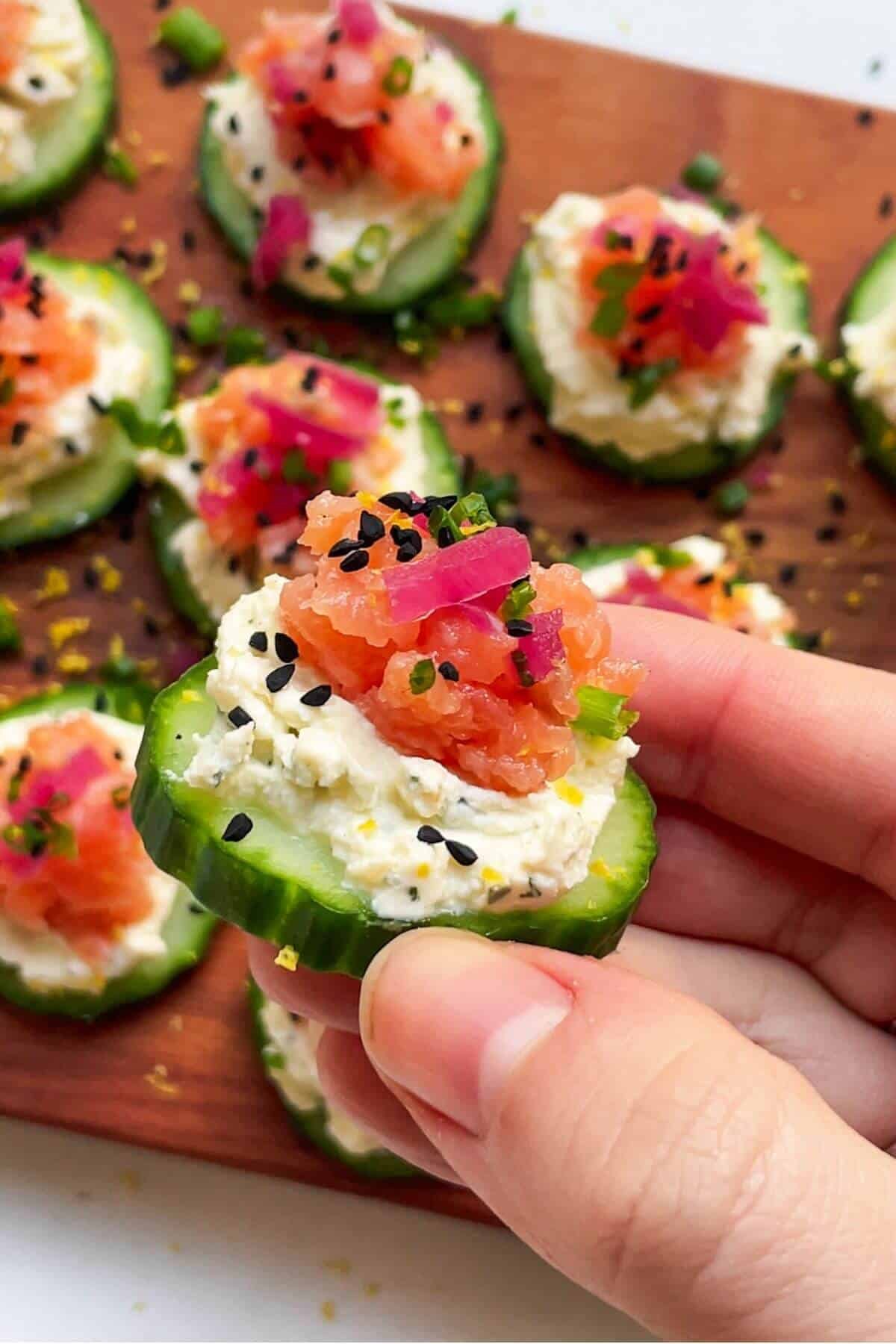Close up of hand holding up smoked salmon cucumber bite.