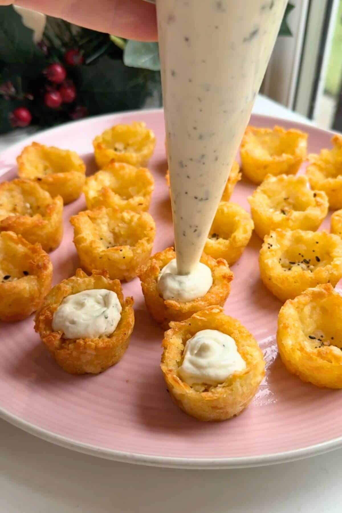 Hash brown cups on a plate, filling being piped inside.