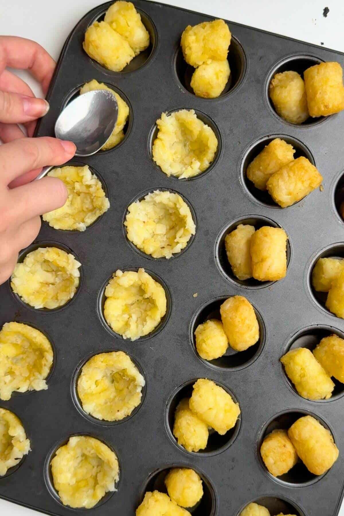 Teaspoon pressing tater tots into cups in muffin pan.