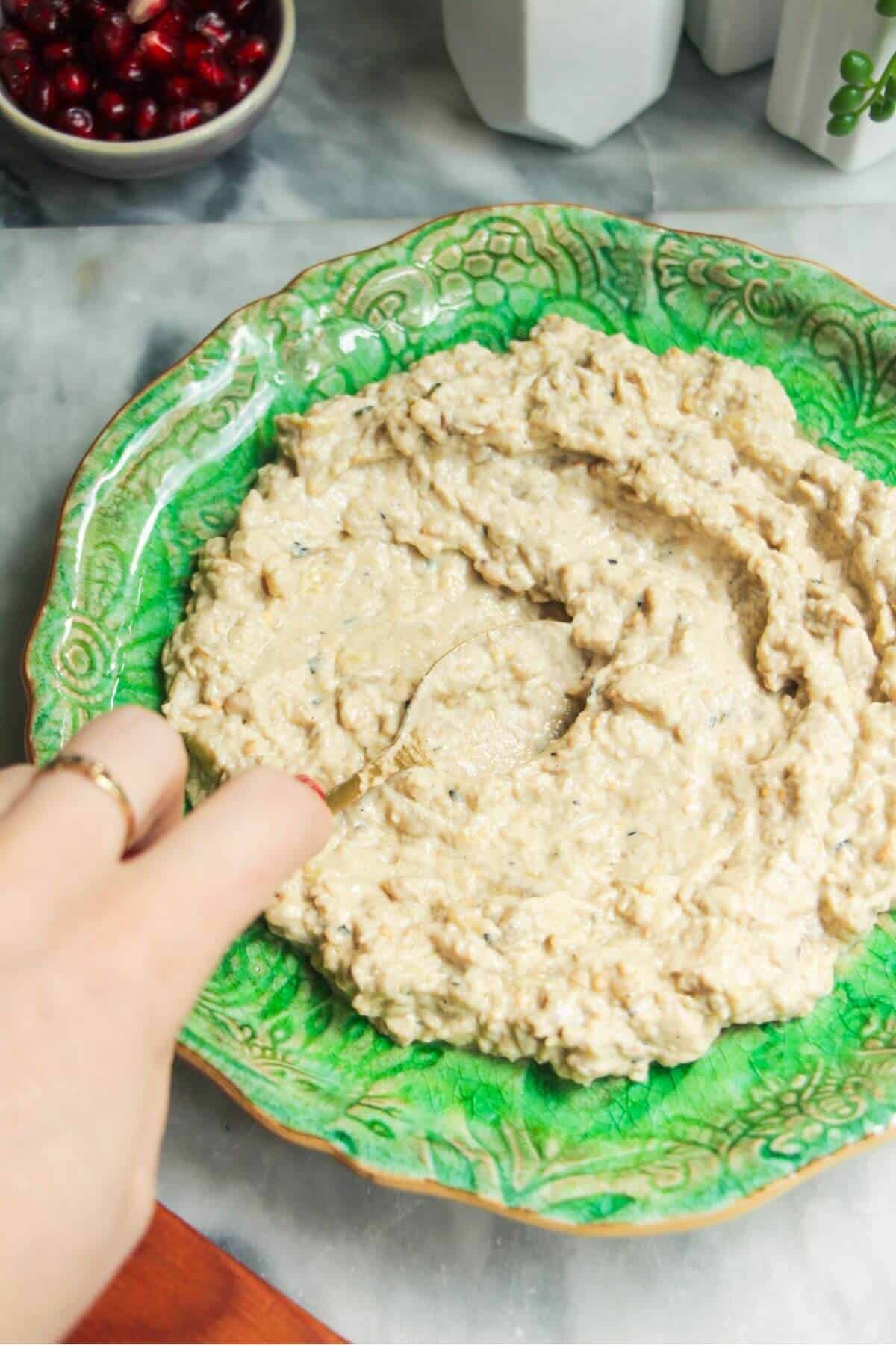 Hand smoothing smoky eggplant dip onto a small green plate.