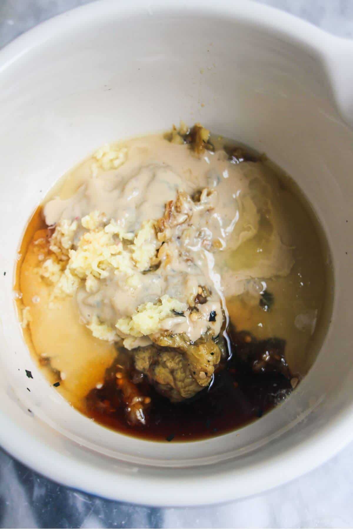 Ingredients for smoky eggplant dip in a white mixing bowl.