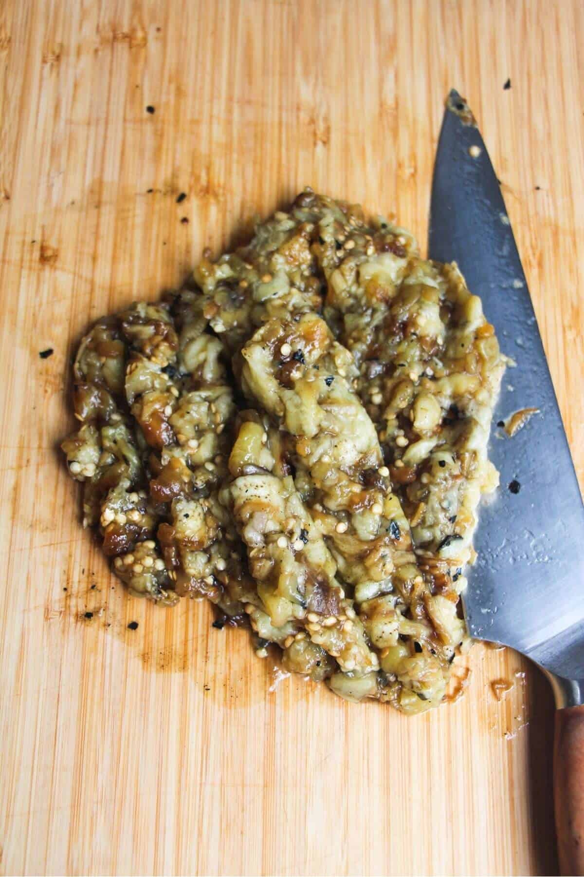 Chopped eggplant on a wooden board with a large knife on the side.