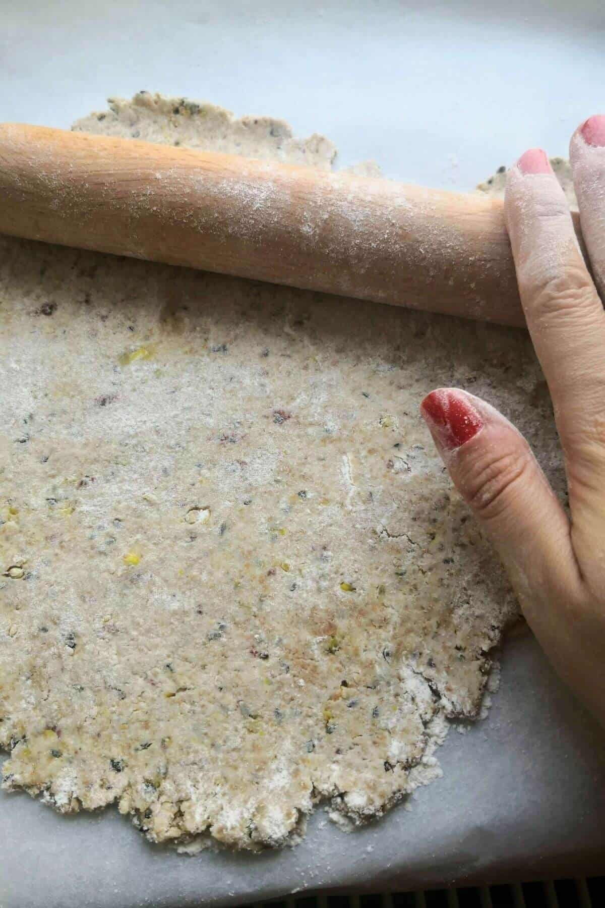 Close up of hands rolling out sourdough discard crackers with a wooden rolling pin.